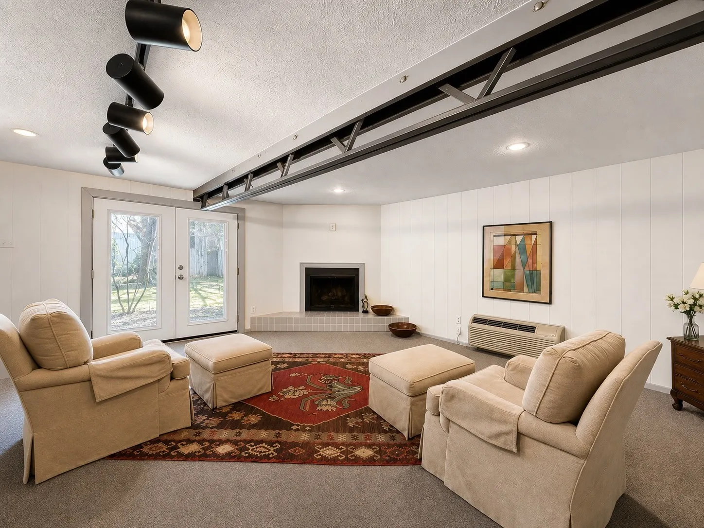 Corner fireplace with tile hearth, recessed lighting, track lighting, exposed ceiling beam, and French doors