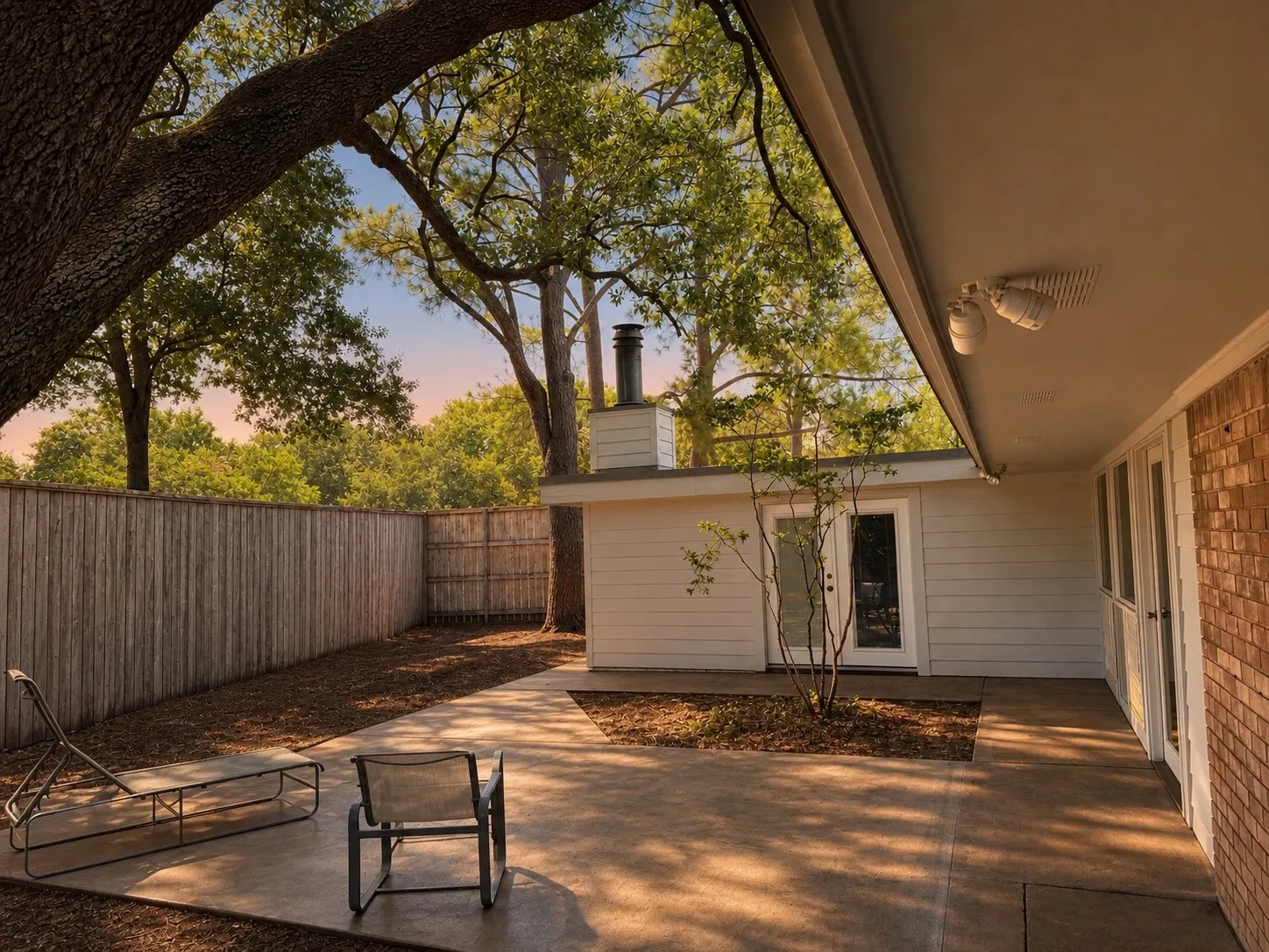Expansive concrete patio with direct access to interior spaces, bordered by a privacy fence, with a separate exterior building featuring a single glass-paneled door