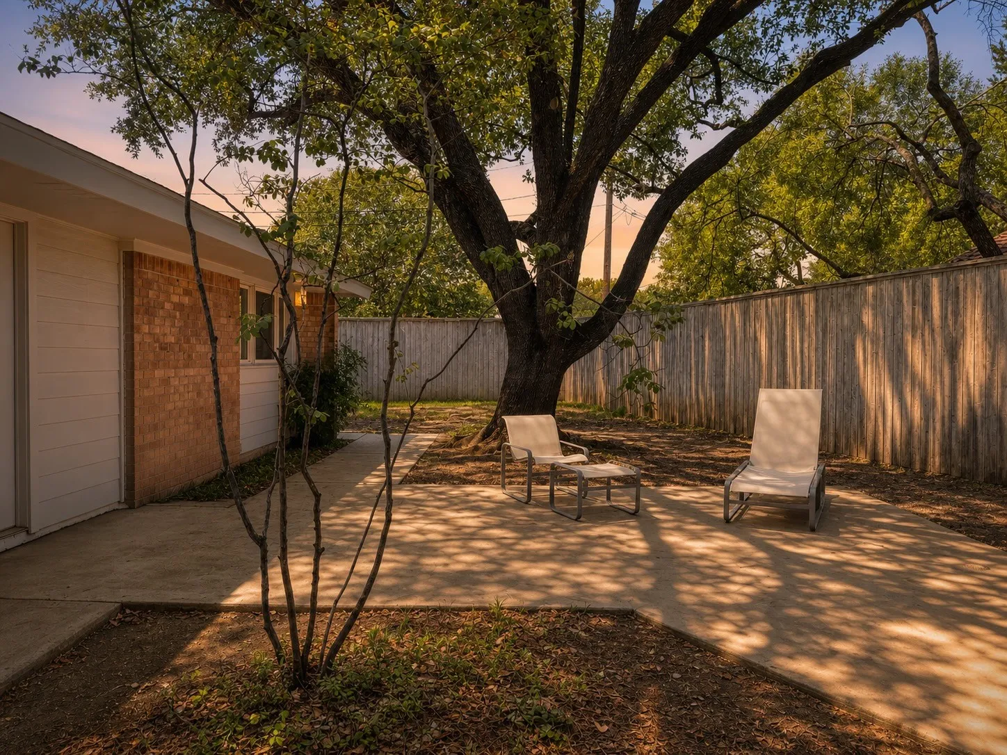 Expansive outdoor patio with mature trees, a wood privacy fence, and brick and siding​​‌​​​​‌​​‌‌​‌‌​​​‌‌​‌​‌​‌​​​‌​​ exterior