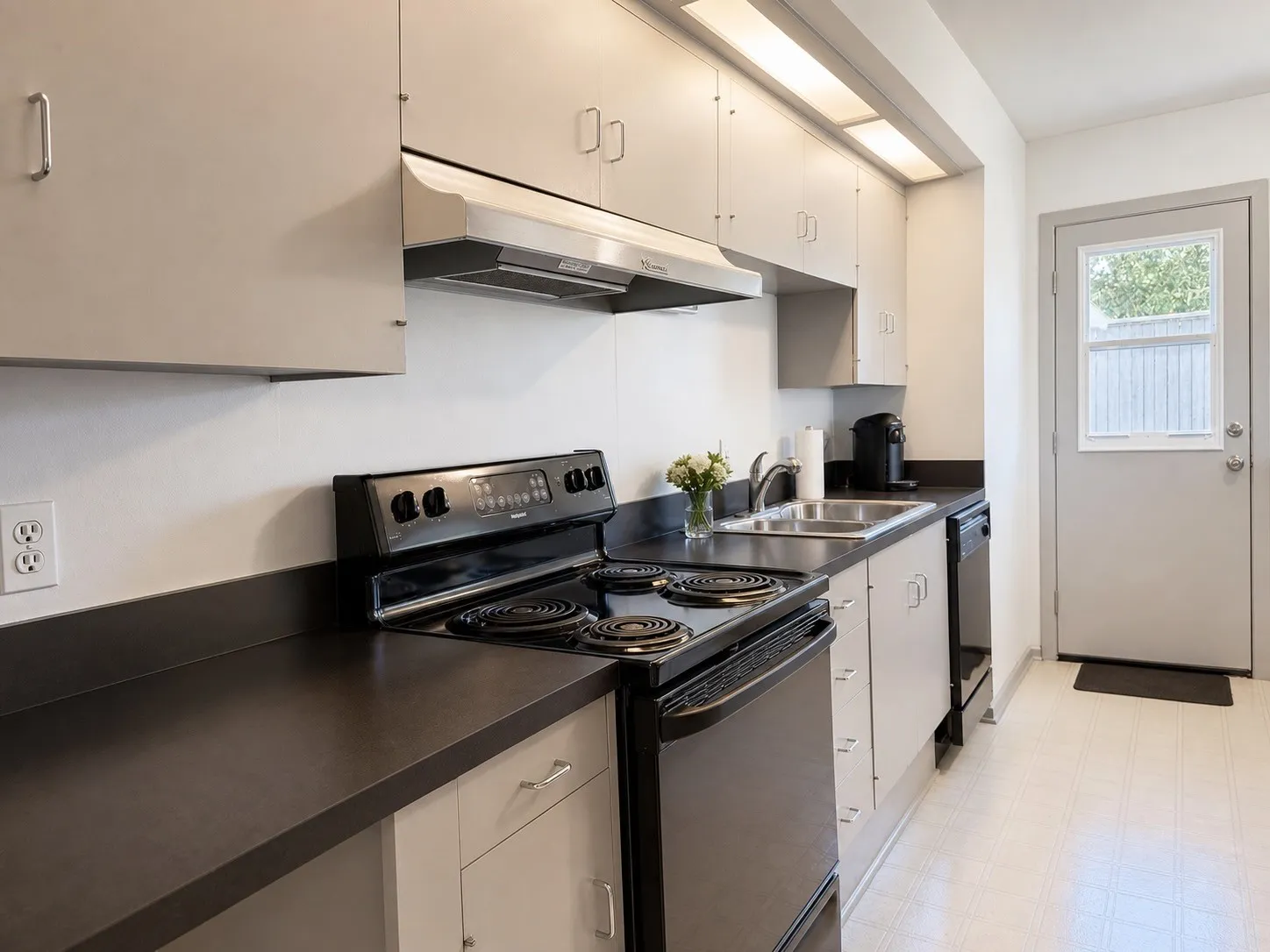 Kitchen featuring a full suite of black appliances, double basin stainless steel sink, ample cabinetry, and durable countertops