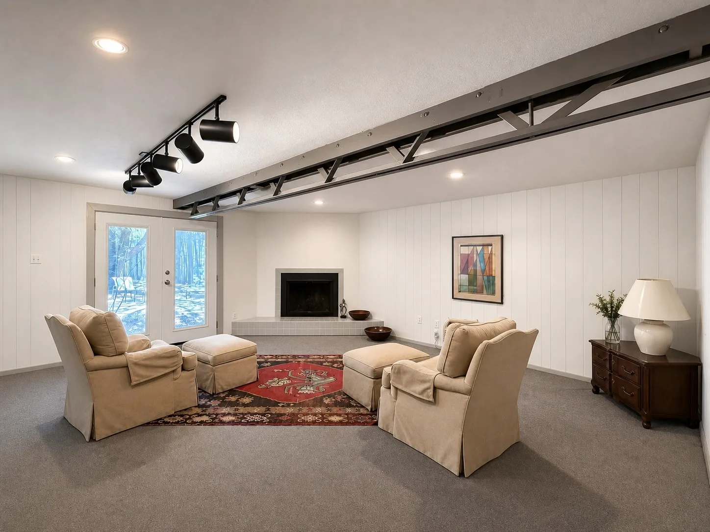 Recessed lighting, exposed structural beam, white paneled walls, built-in fireplace with hearth, and exterior french doors