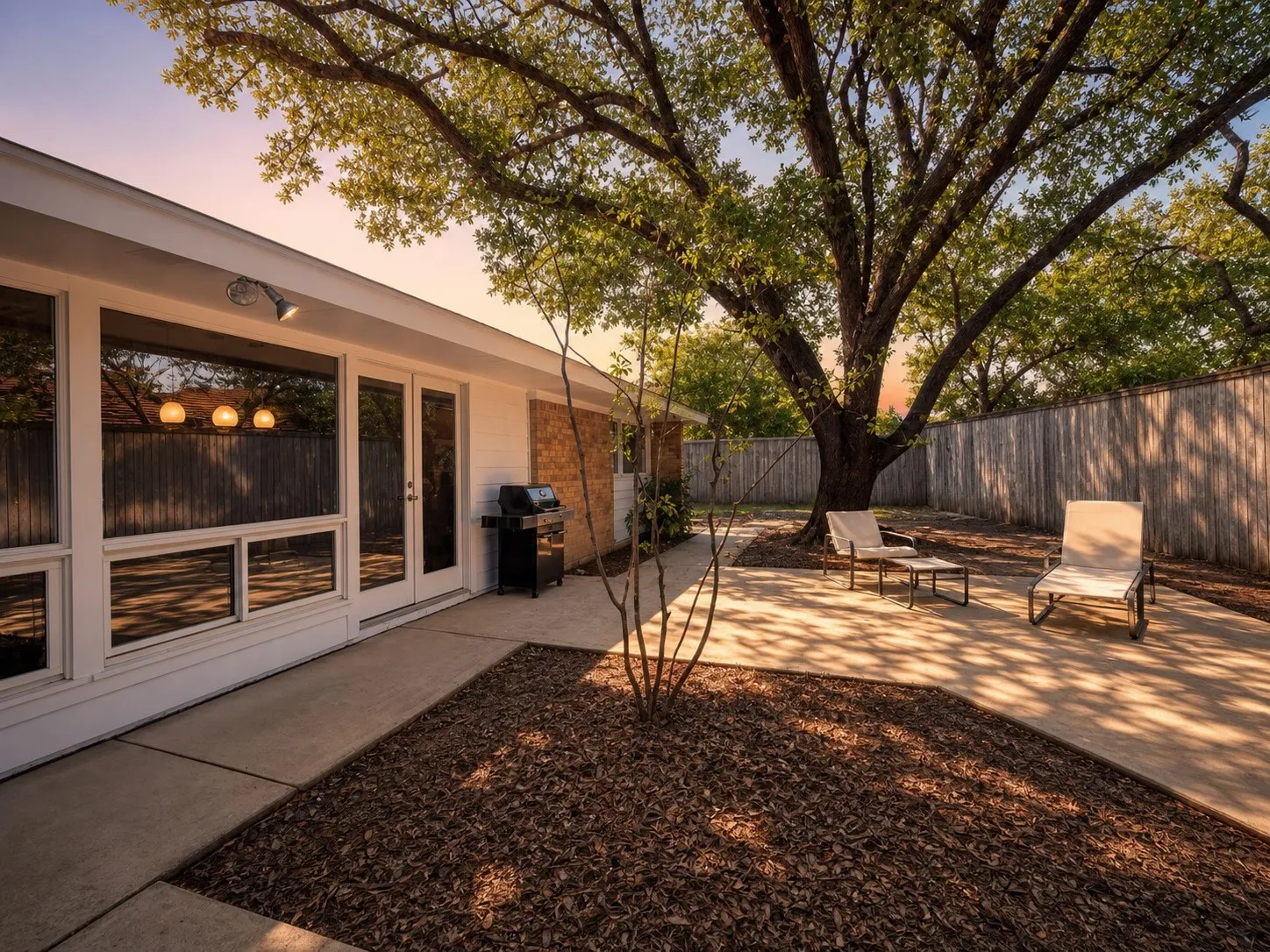 Expansive concrete patio with mature tree, wood fence, and large window panels