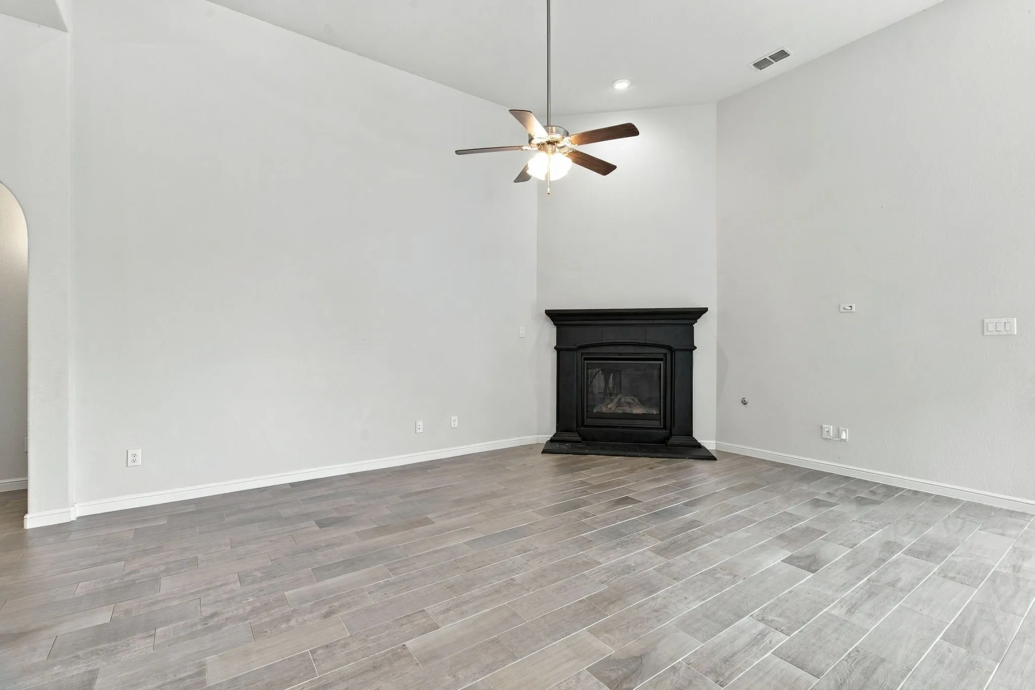 Vaulted ceiling featuring a ceiling fan, corner fireplace with a black mantel, and wood-look flooring