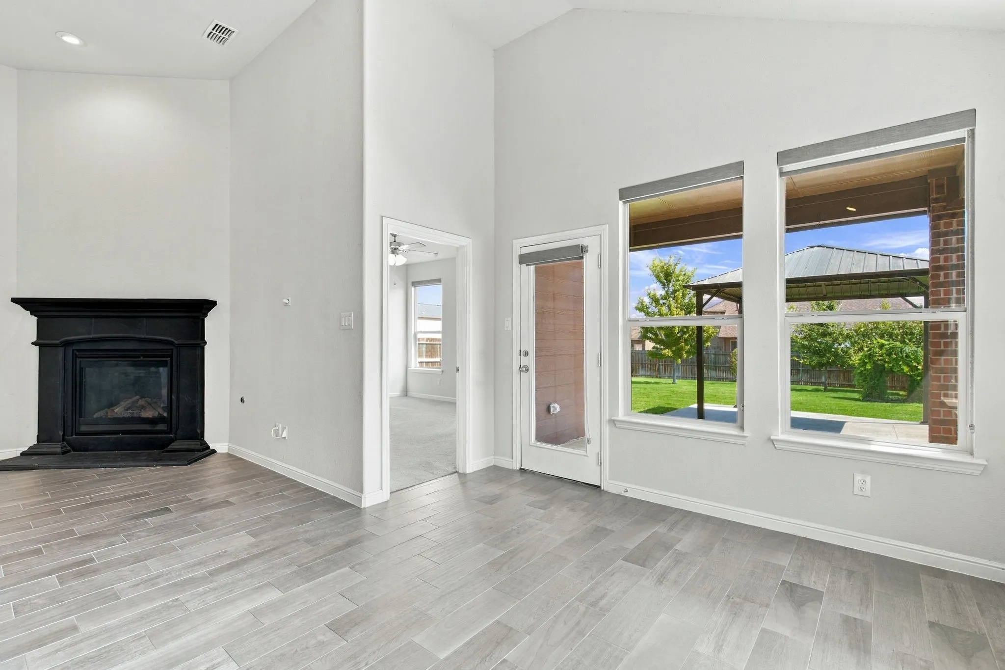 Vaulted ceilings with recessed lighting, black fireplace with mantel, wood-finish tile flooring, multiple windows, and a glass-paneled exterior door