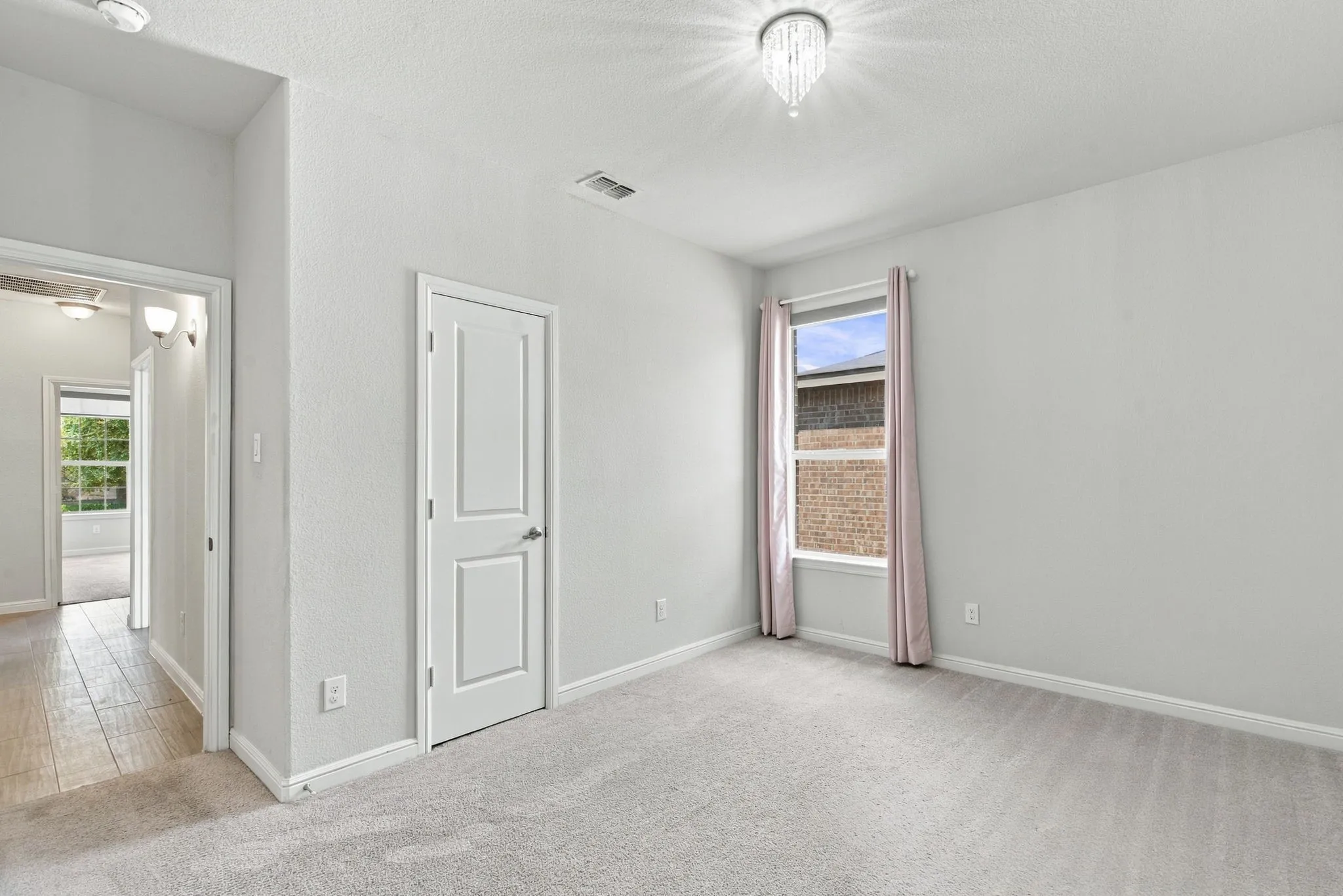 Plush carpeting, a modern crystal chandelier, a window with drapery, and a white paneled door