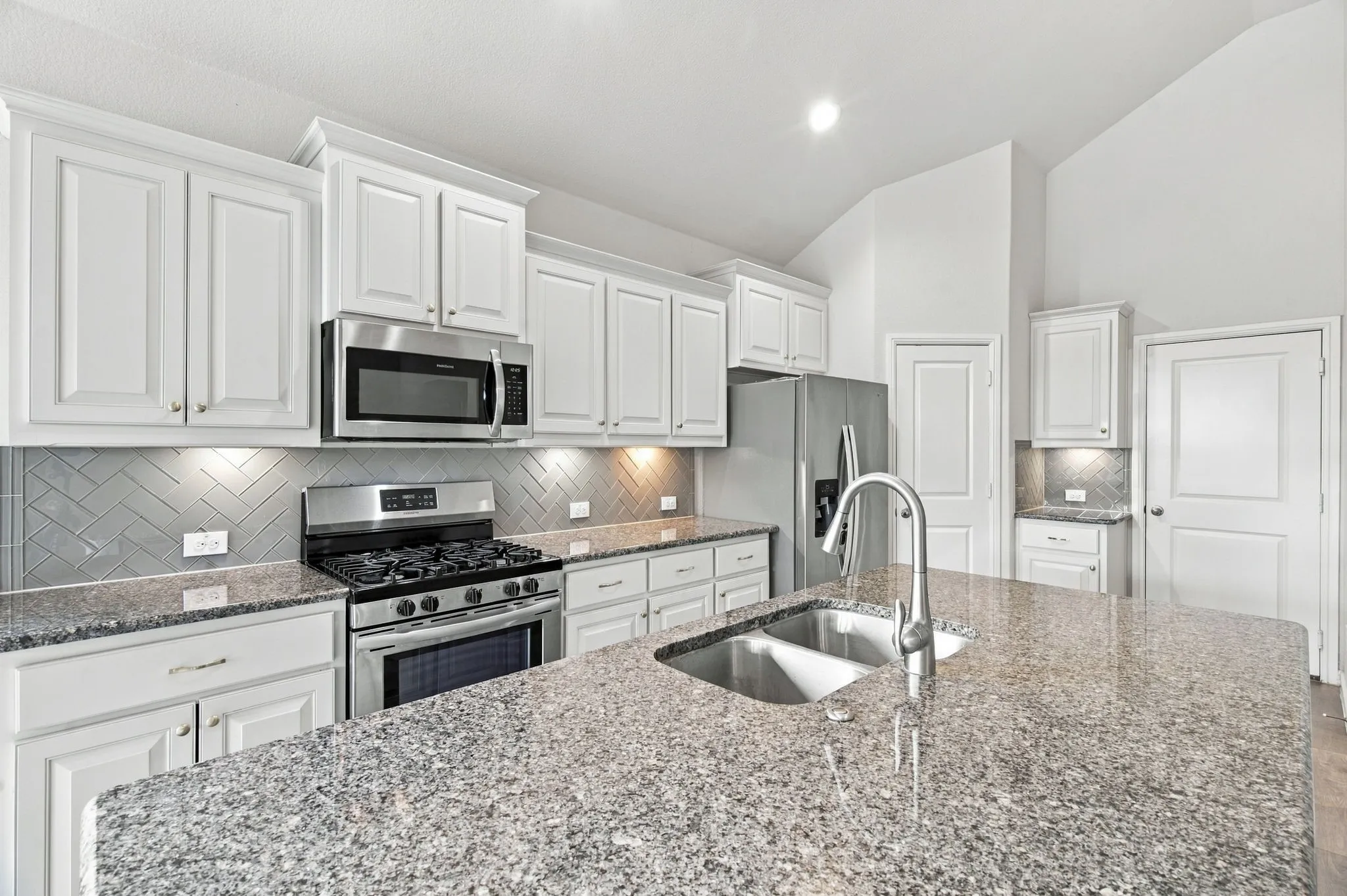 Kitchen featuring white cabinetry, stainless steel appliances, granite countertops, a herringbone tile backsplash, and a double basin sink with a gooseneck faucet