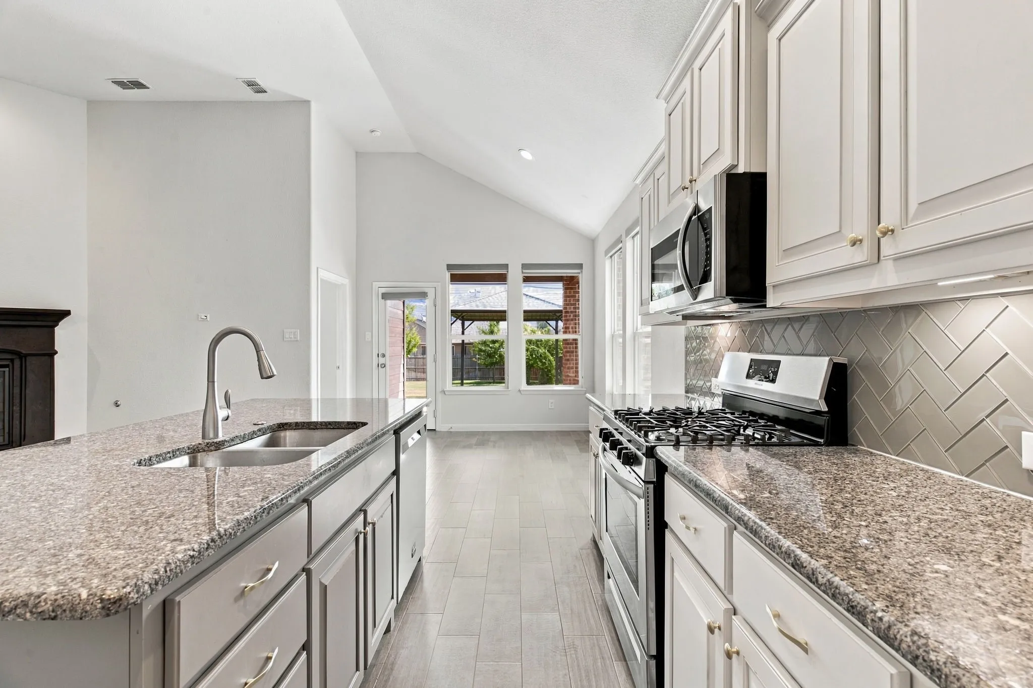 Kitchen featuring light-finish cabinetry, granite countertops, stainless steel appliances, and a herringbone tile backsplash