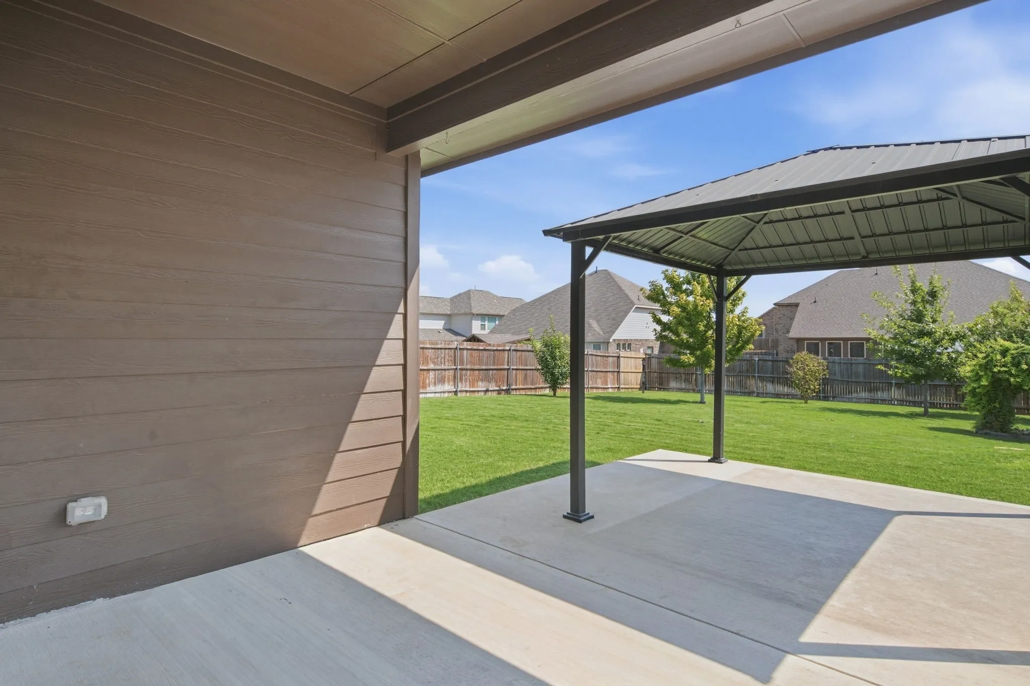 Covered patio with a concrete surface, expansive lawn, and a detached gazebo