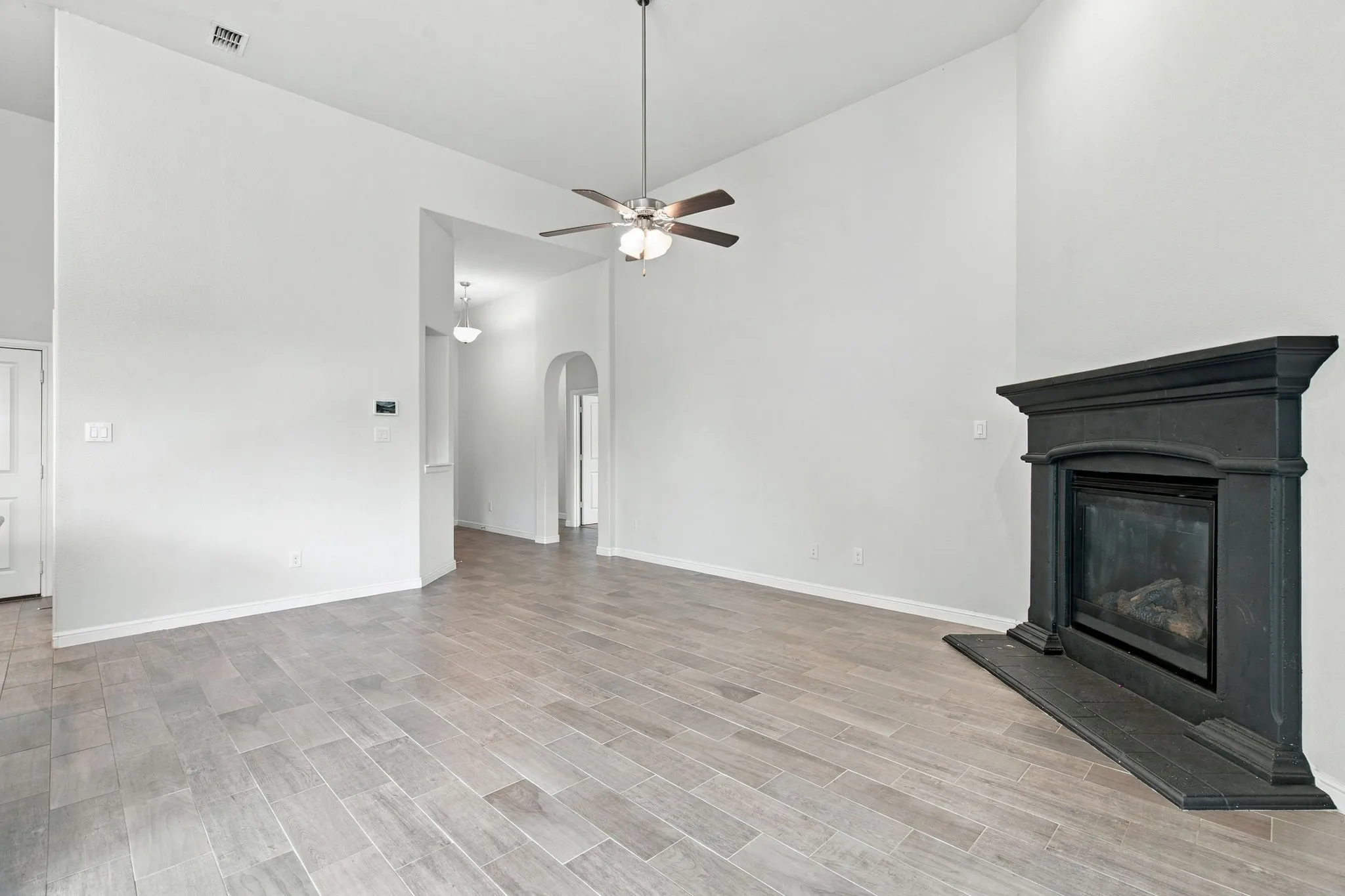 Spacious room featuring vaulted ceilings, wood-finish tile flooring, a dark-toned fireplace with mantel, and an overhead ceiling fan