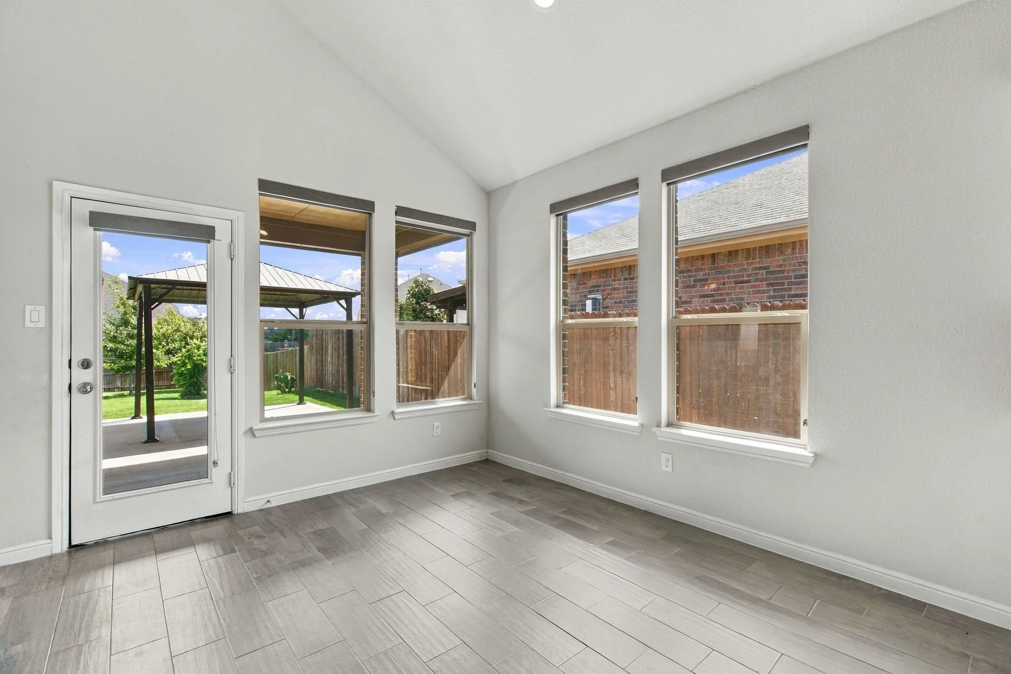 Vaulted ceiling, wood-finish flooring, multiple windows, full-light door, and a covered patio structure