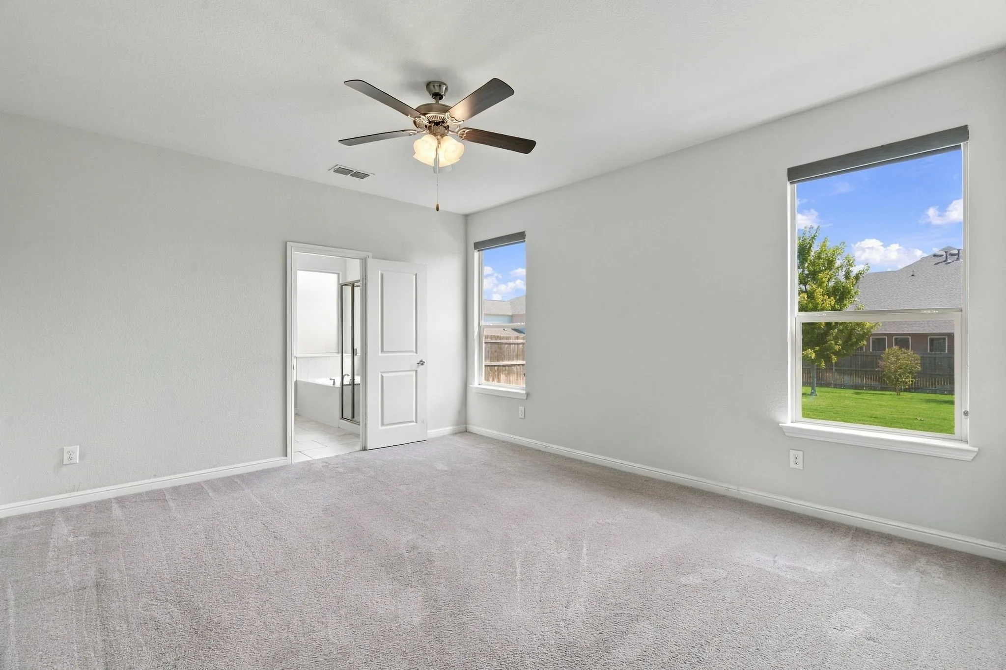 Recessed ceiling with a fan light fixture, two windows with roller shades, and light gray wall paint