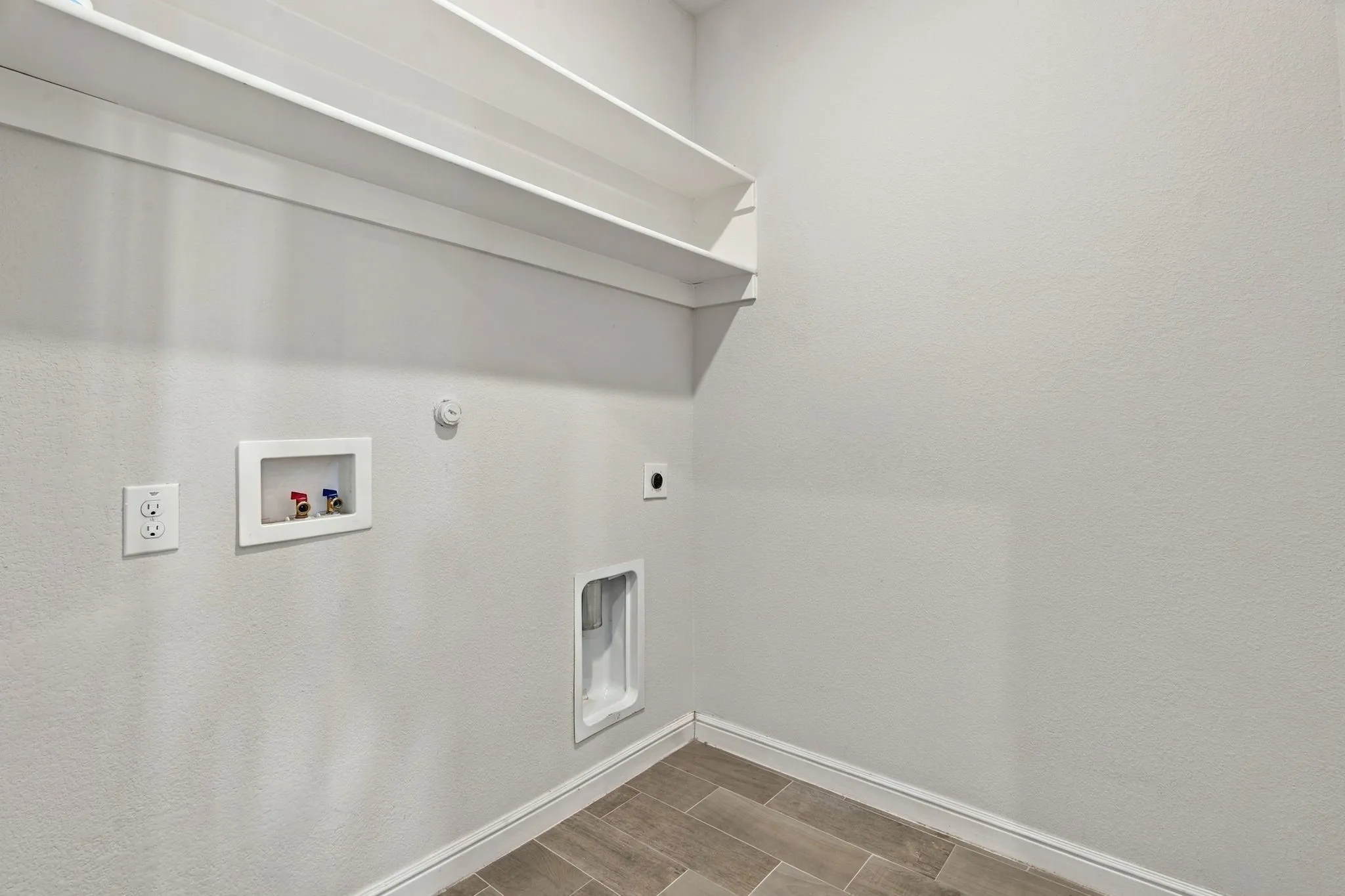 Laundry area featuring a textured wall finish, wood-finish flooring, two white built-in shelves, and white trim