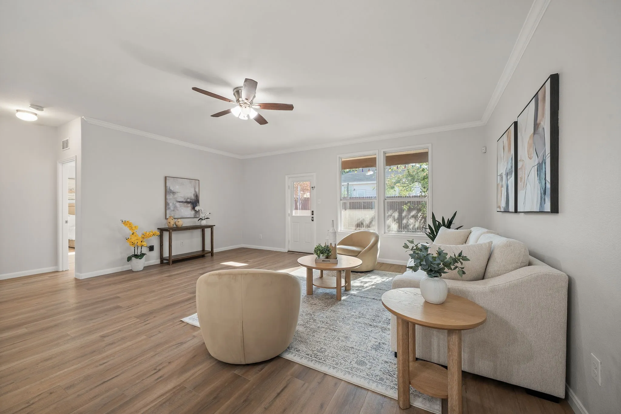 Wood-finish flooring throughout, ceiling fan with integrated lighting, crown molding, and a rear door with an upper window