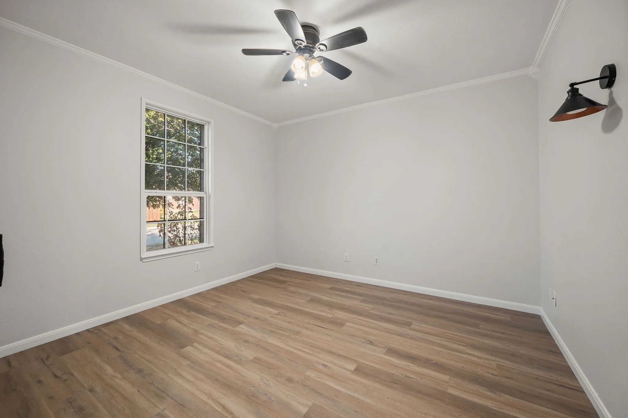 Wood-finish flooring with crown molding, a ceiling fan, and a wall-mounted sconce