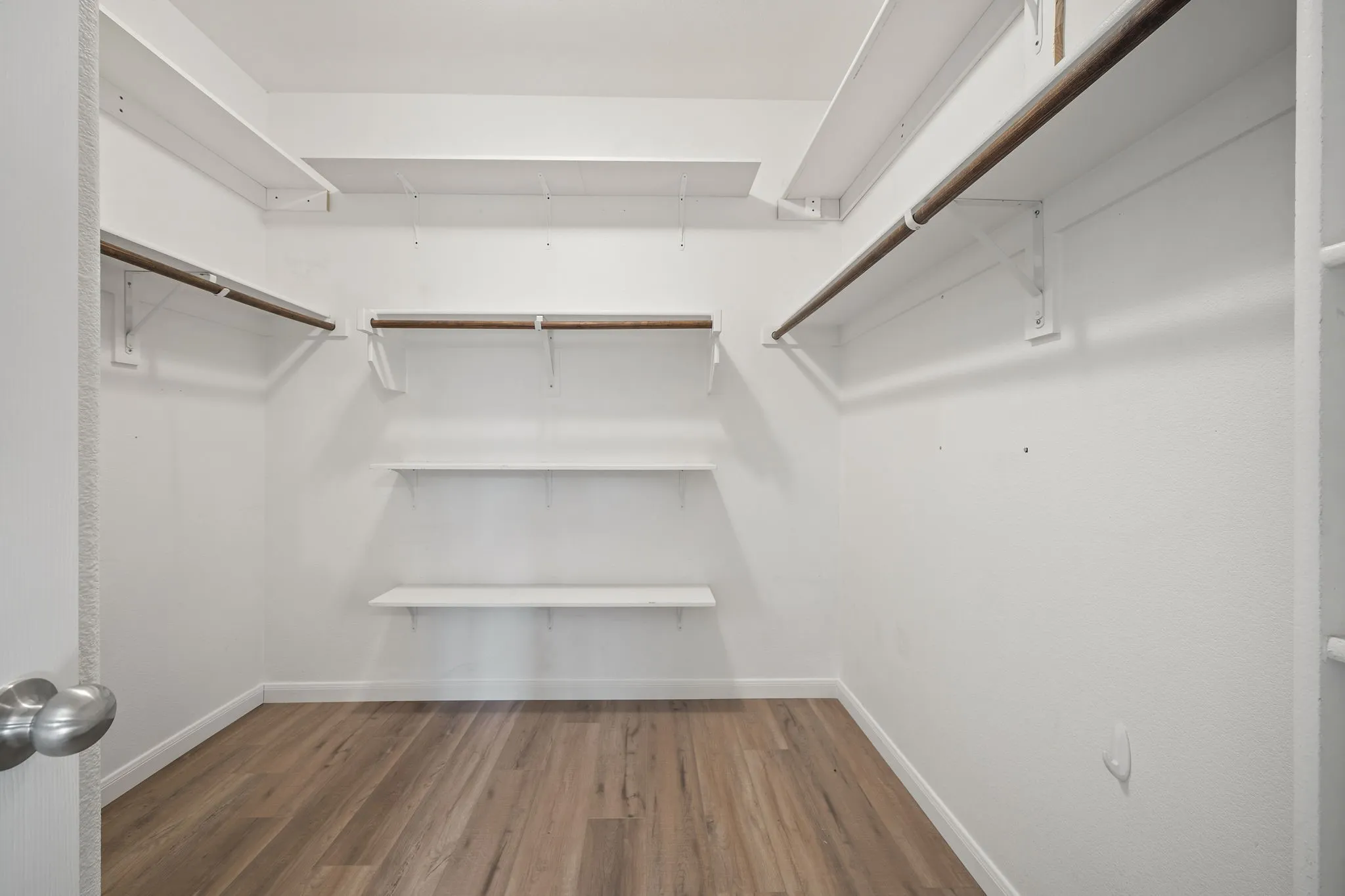 Walk-in closet with wood-finish flooring, white walls, and multiple white shelving units
