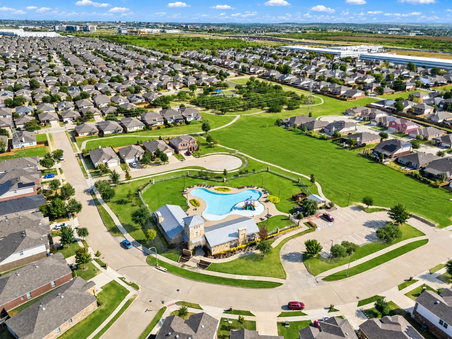 Community club building with a swimming pool, adjacent recreational green space, and paved walking paths