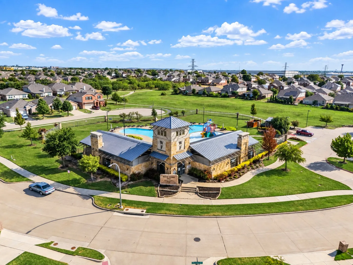 Community amenity center featuring a stone exterior, tower element, multiple pools, and surrounding green spaces
