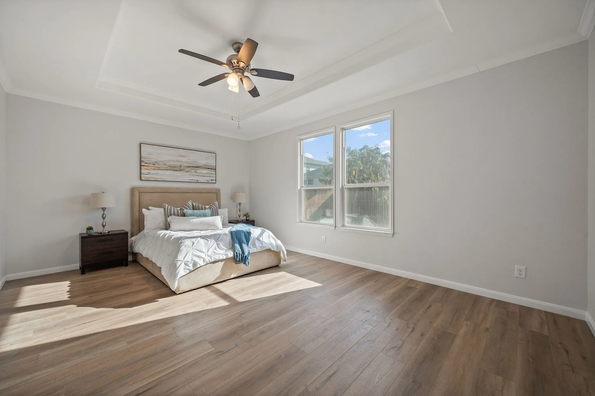 Room featuring wood-finish flooring, a tray ceiling with a ceiling fan, and two windows