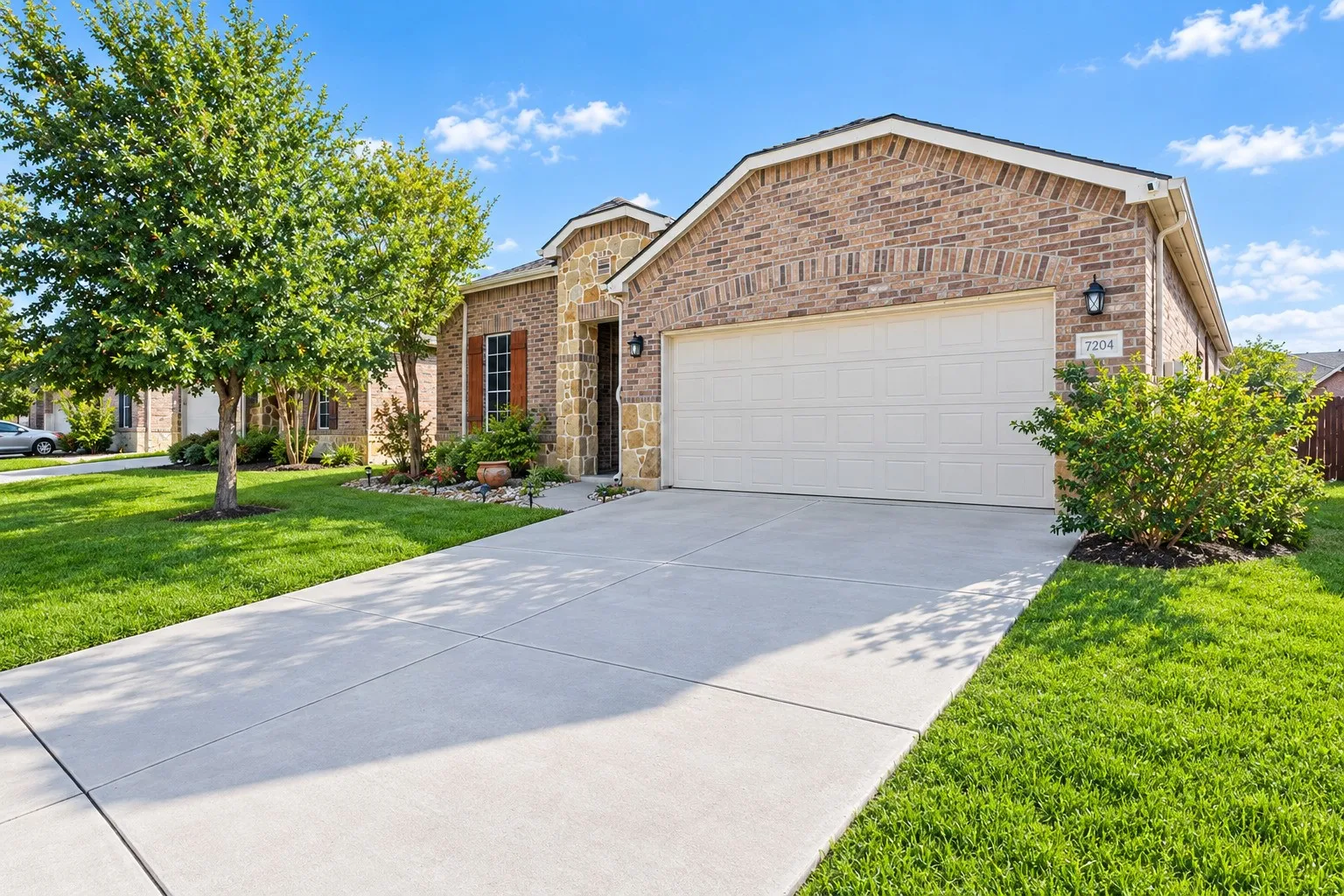 Brick exterior with stone accents, attached garage, concrete driveway, and established front landscaping