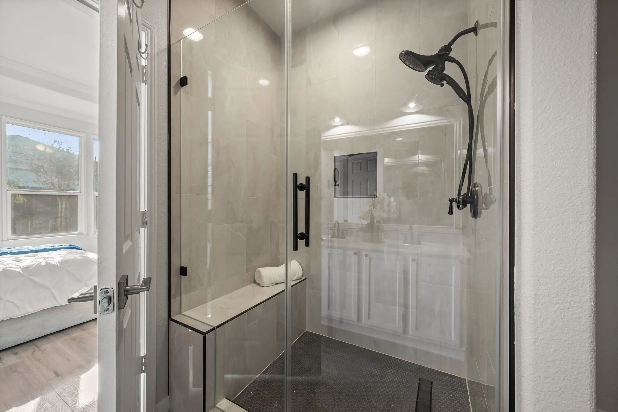 Glass-enclosed shower with a built-in bench, dark-toned shower fixtures, and mosaic floor tile