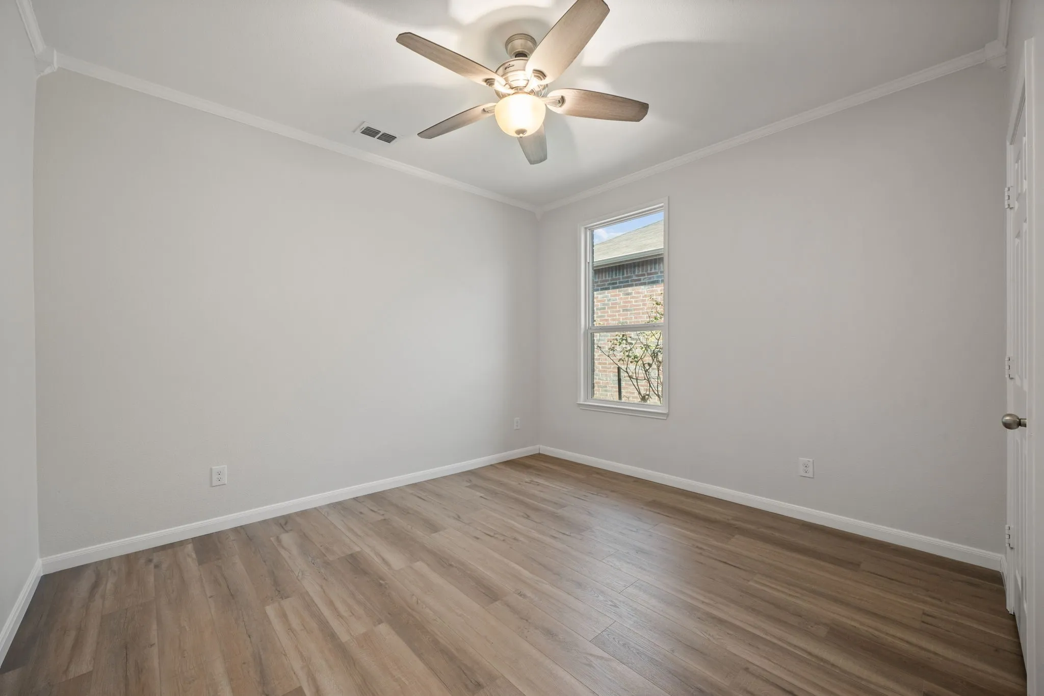 Wood-finish flooring, single window, ceiling fan with integrated lighting, crown molding, and painted interior walls