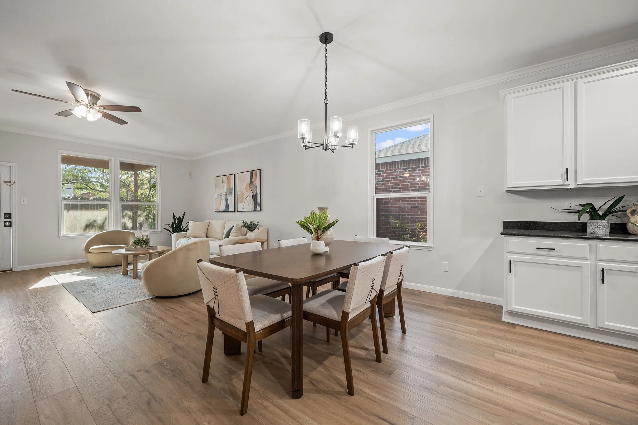 Wood-finish flooring throughout, white cabinetry with dark hardware, dark countertops, and a ceiling fan