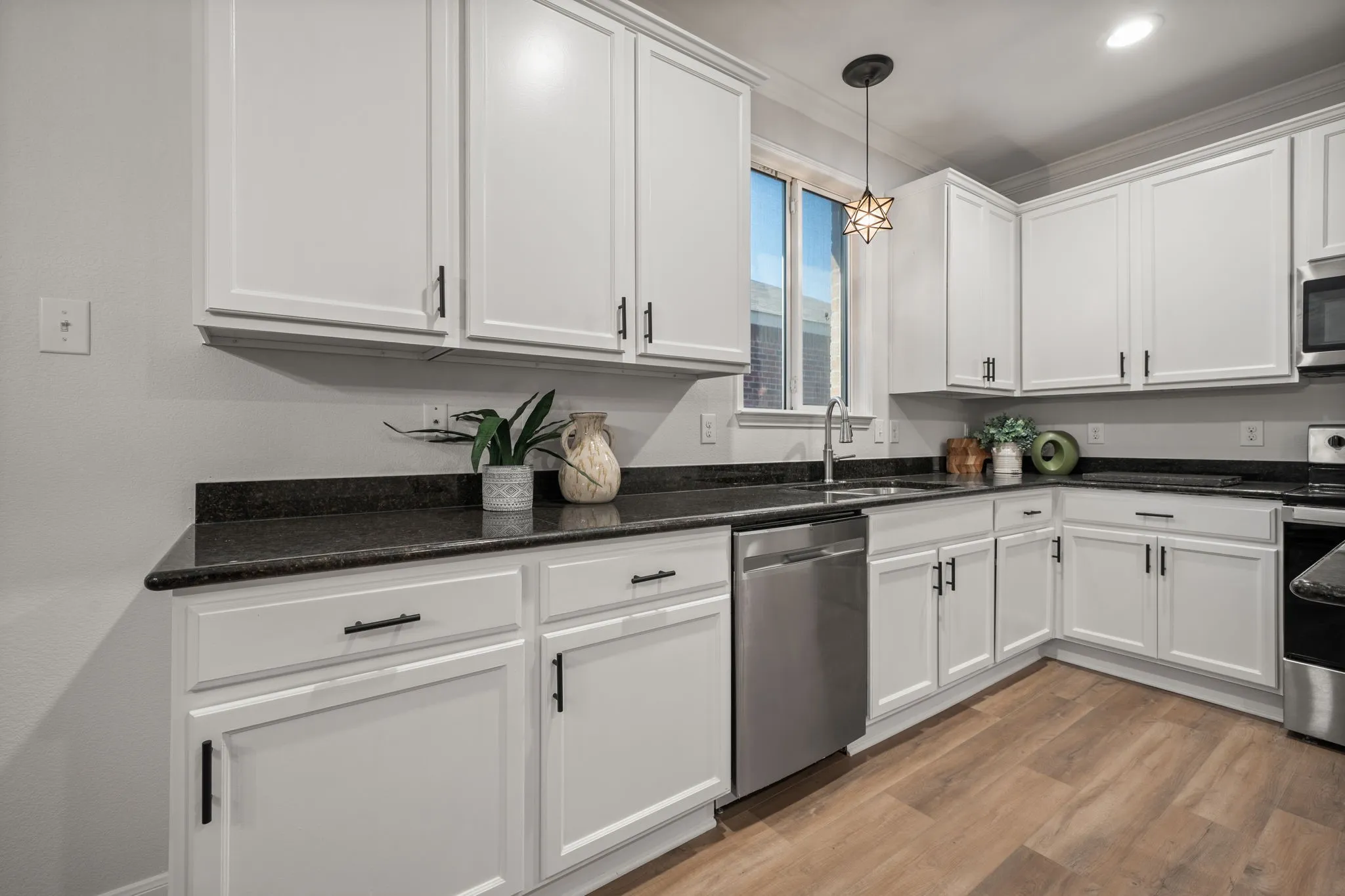 White cabinetry with matte black hardware, dark countertops, a stainless steel dishwasher, a stainless steel sink with a gooseneck faucet, and wood-finish flooring