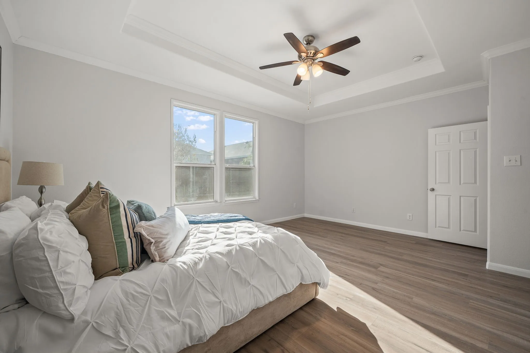 Tray ceiling with crown molding, wood-finish flooring, ceiling fan with integrated lighting, and white paneled door