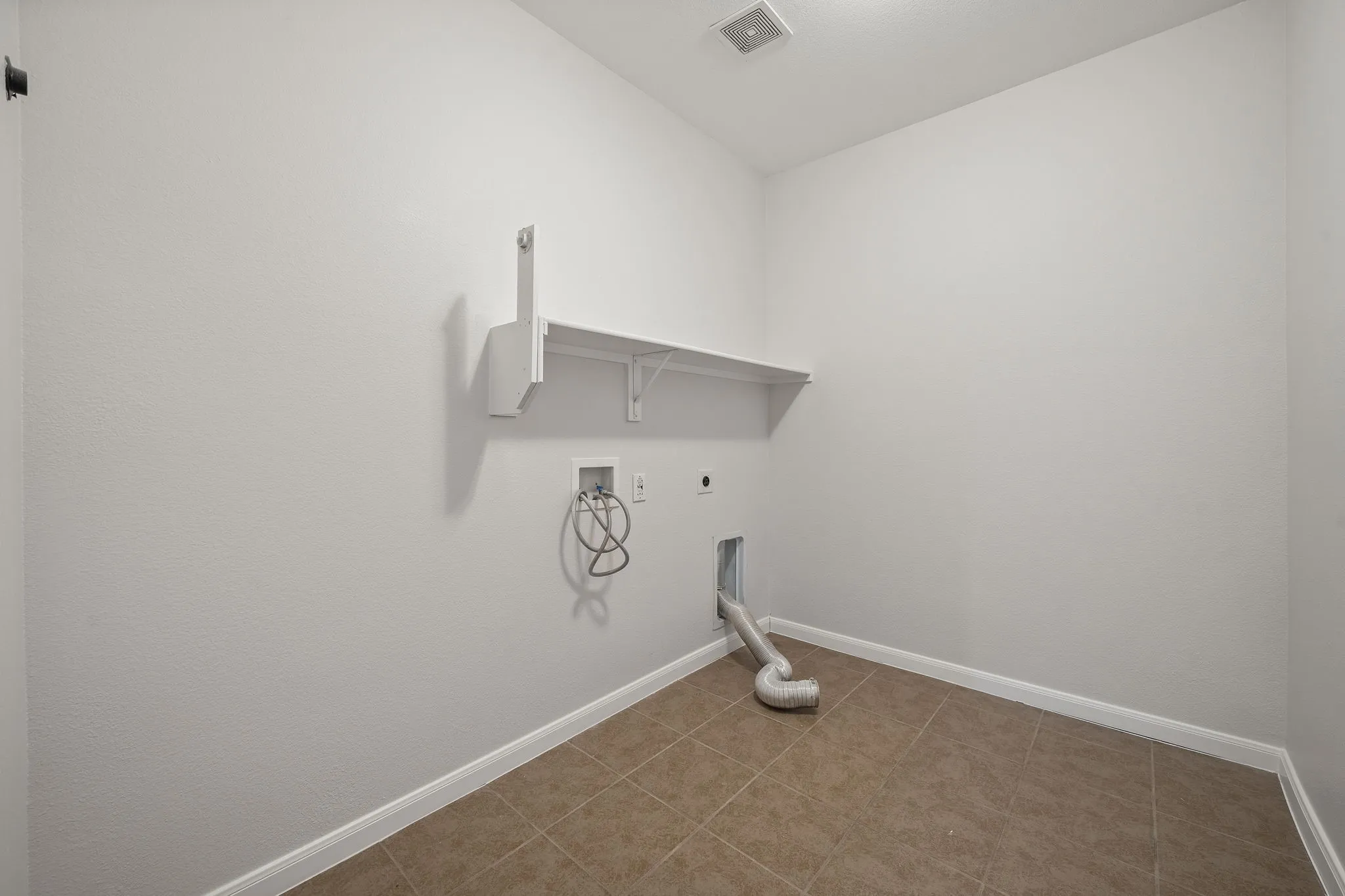 Utility room with neutral tile flooring, light-toned walls, and a built-in shelf