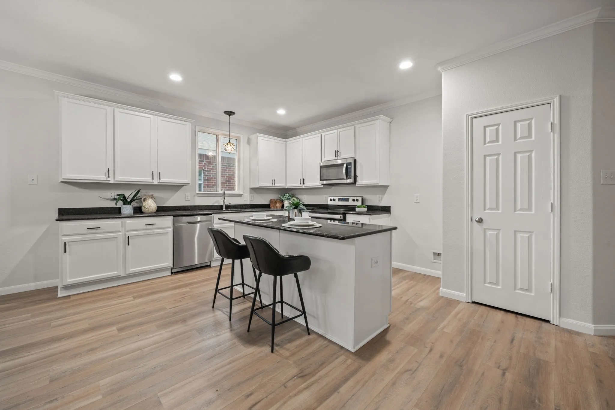 Open kitchen featuring a central island, white cabinetry, dark countertops, wood-finish flooring, and stainless steel appliances