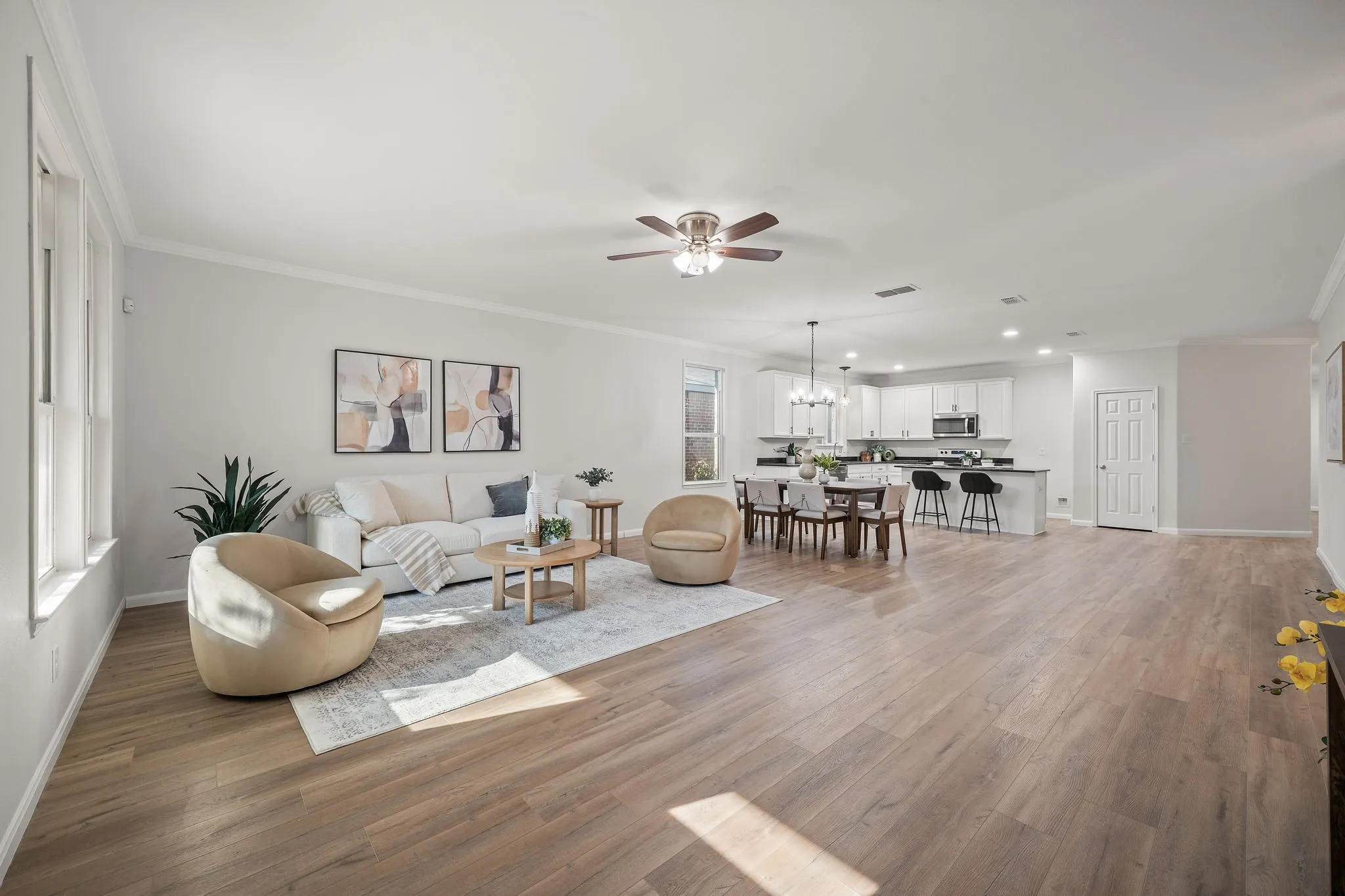 Open-concept living area with wood-finish flooring, a ceiling fan, and crown molding