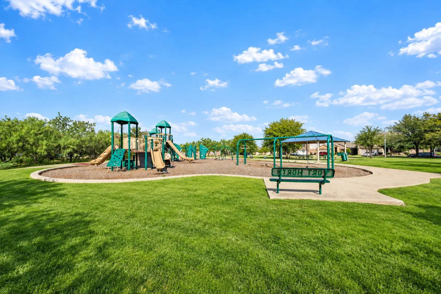 Expansive green space featuring a playground with multiple slides and climbing structures, a swing set, and a covered seating area