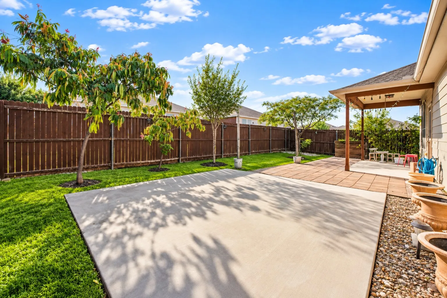 Expansive backyard with a full privacy fence, concrete patio, and separate covered patio with a wood pergola
