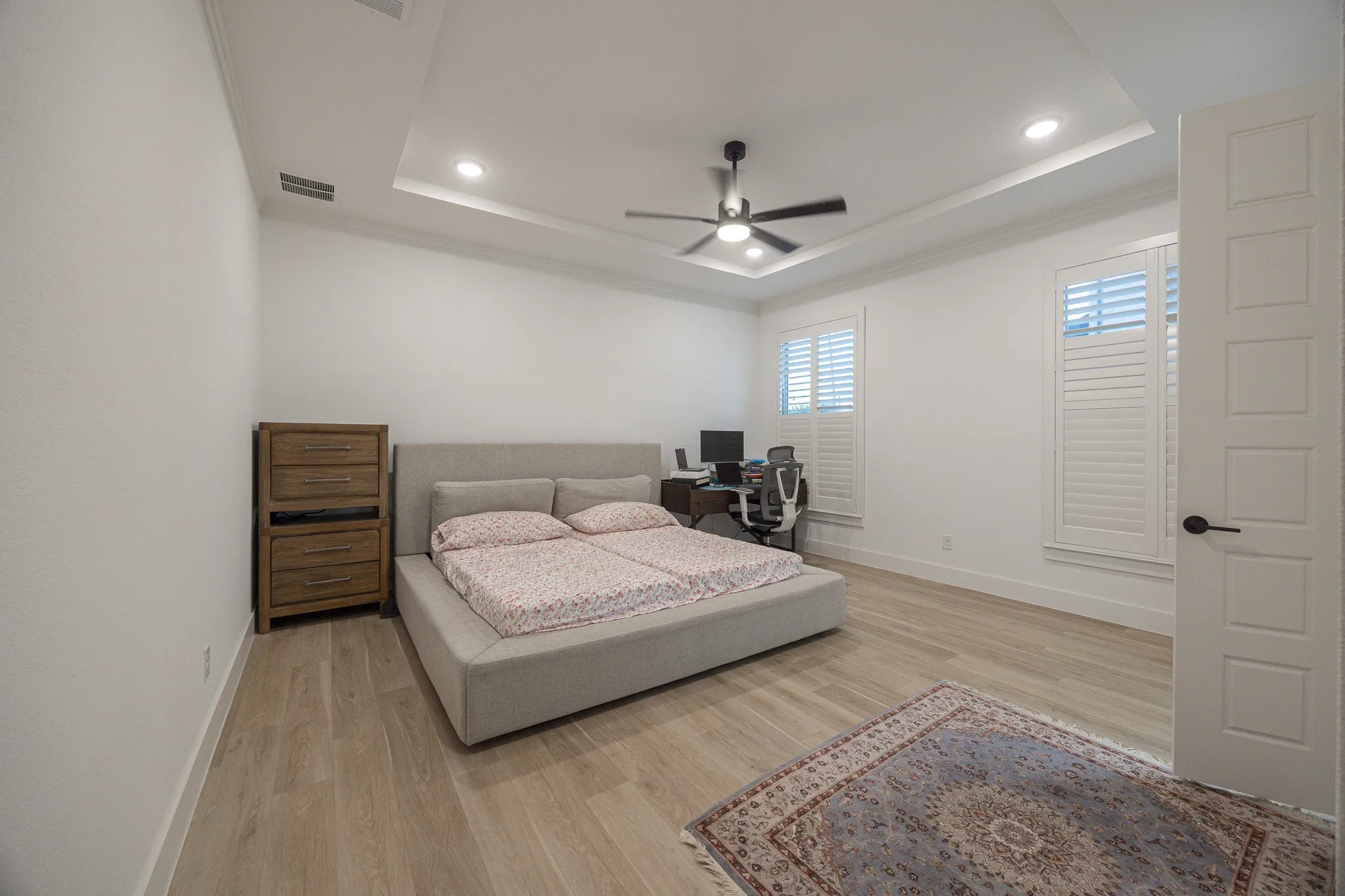 Tray ceiling with recessed lighting and a ceiling fan, light wood-finish flooring, and white plantation shutters