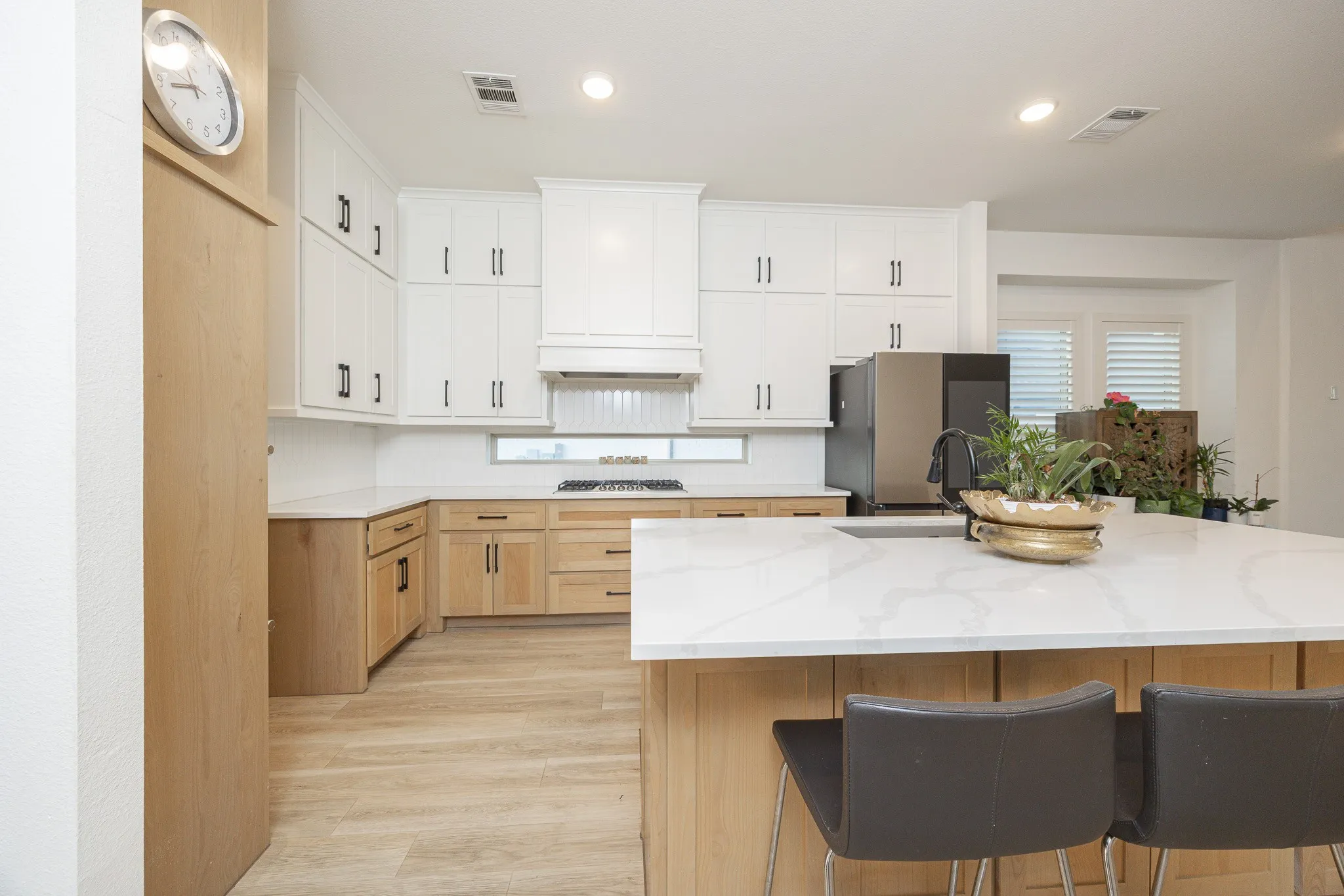 White upper cabinetry with black hardware, natural wood-finish lower cabinetry, light wood-finish flooring, white stone-finish countertops, and a built-in stainless steel appliance