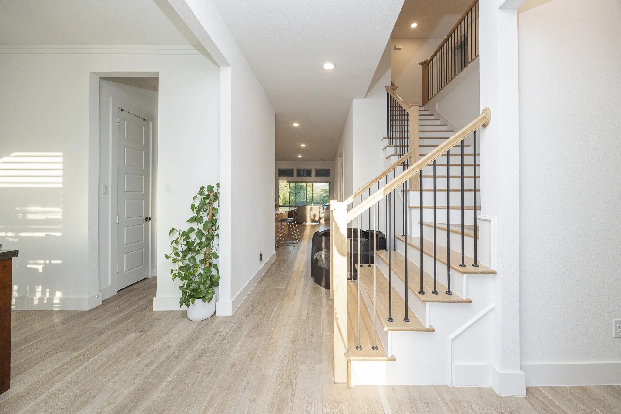 Wood-finish flooring throughout, white painted walls, recessed lighting, and a staircase with natural wood handrails and black metal balusters
