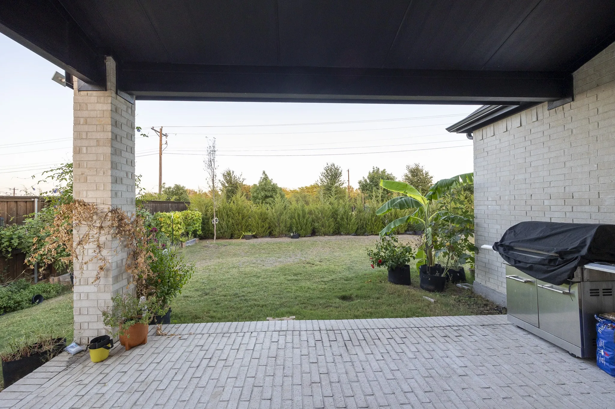 Covered patio with light-toned brick paver flooring, supported by brick columns, leading to a grass lawn
