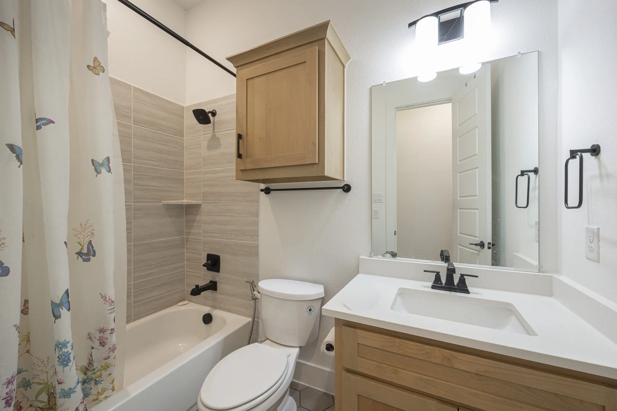 White bathtub with matte black fixtures, light-toned horizontal wall tiling, and a recessed shelf