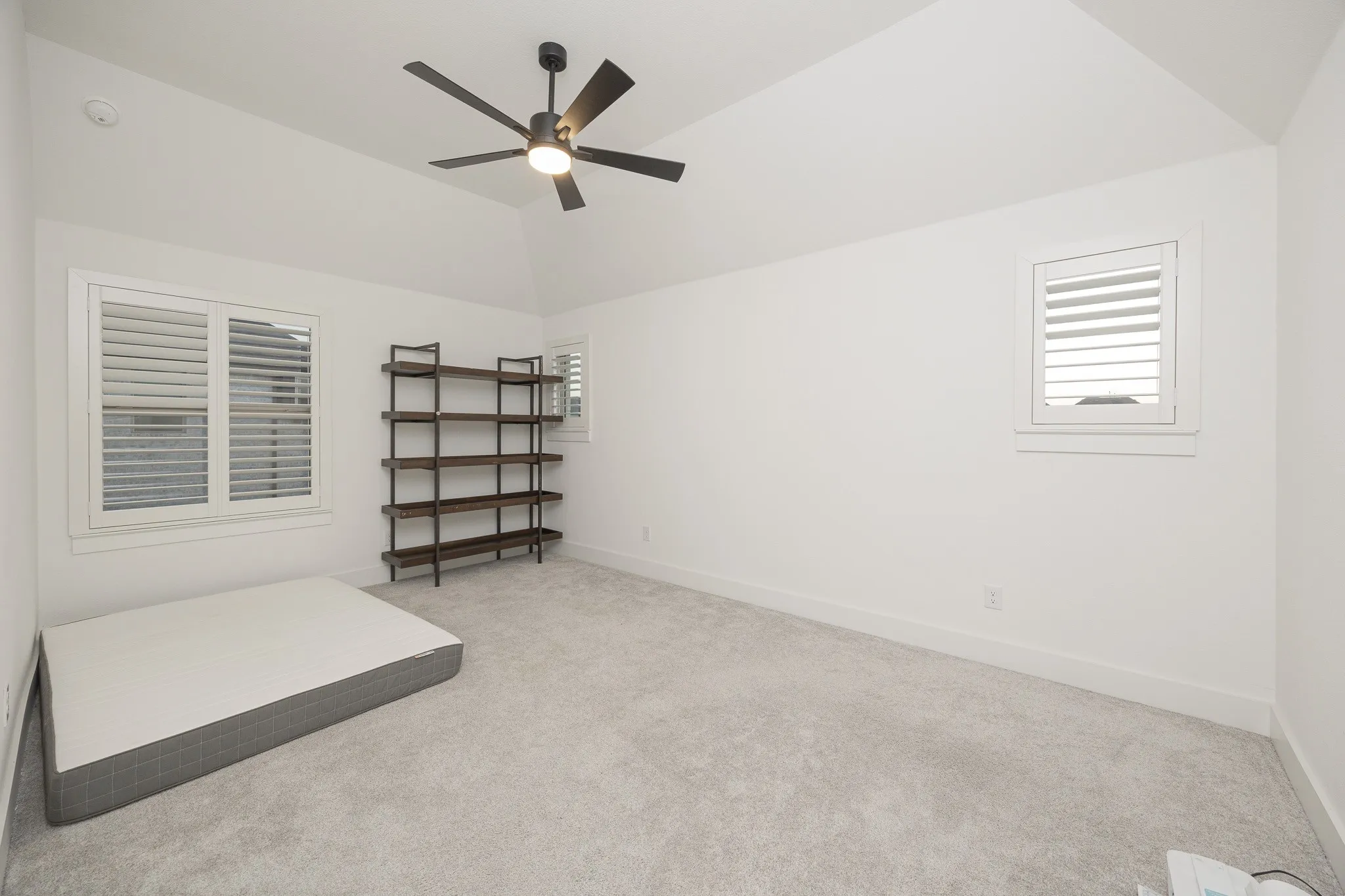 Vaulted ceiling with a matte black ceiling fan, white plantation shutters, and light grey carpeting