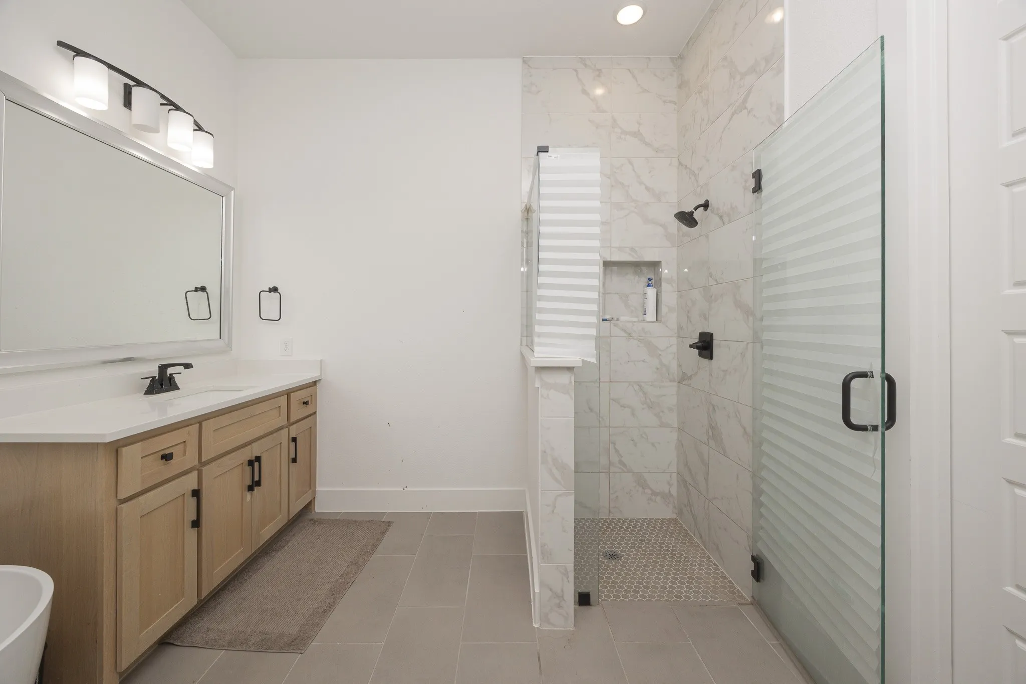 Double vanity with light wood-finish cabinetry, white countertop, and matte black fixtures
