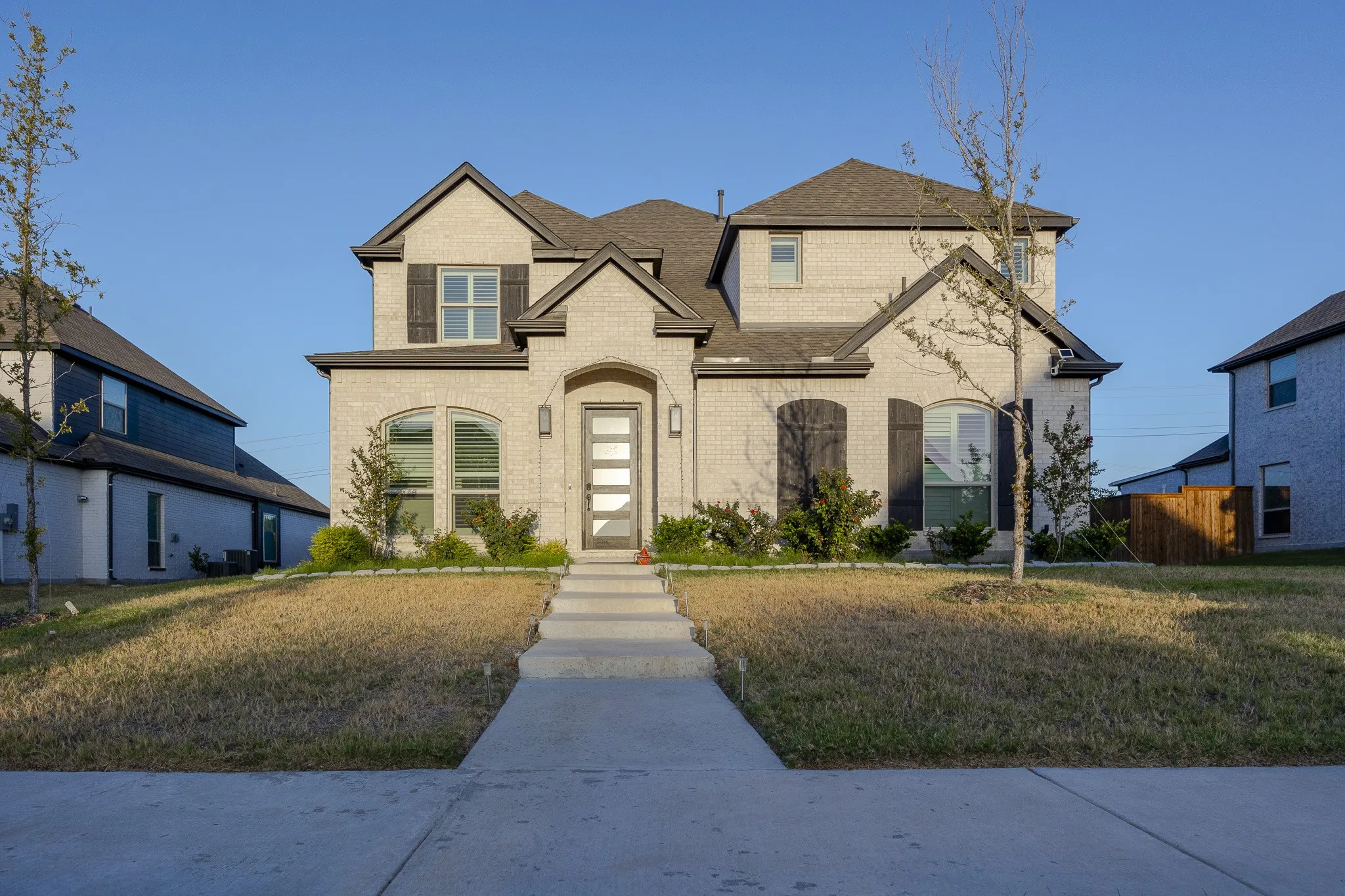 Brick facade residence featuring dark shutters, an arched window, and a multipane front door