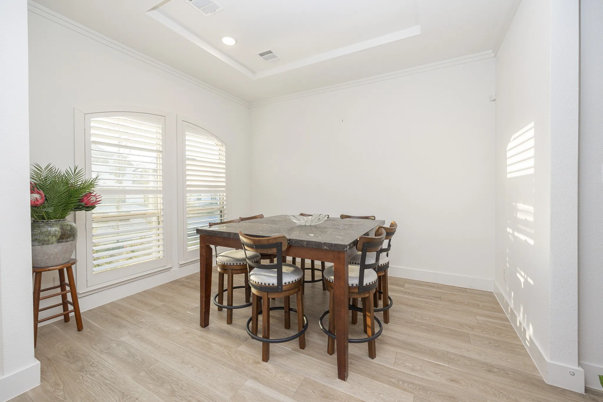 Arched windows with plantation shutters, crown molding, tray ceiling with recessed lighting, and wood-finish flooring