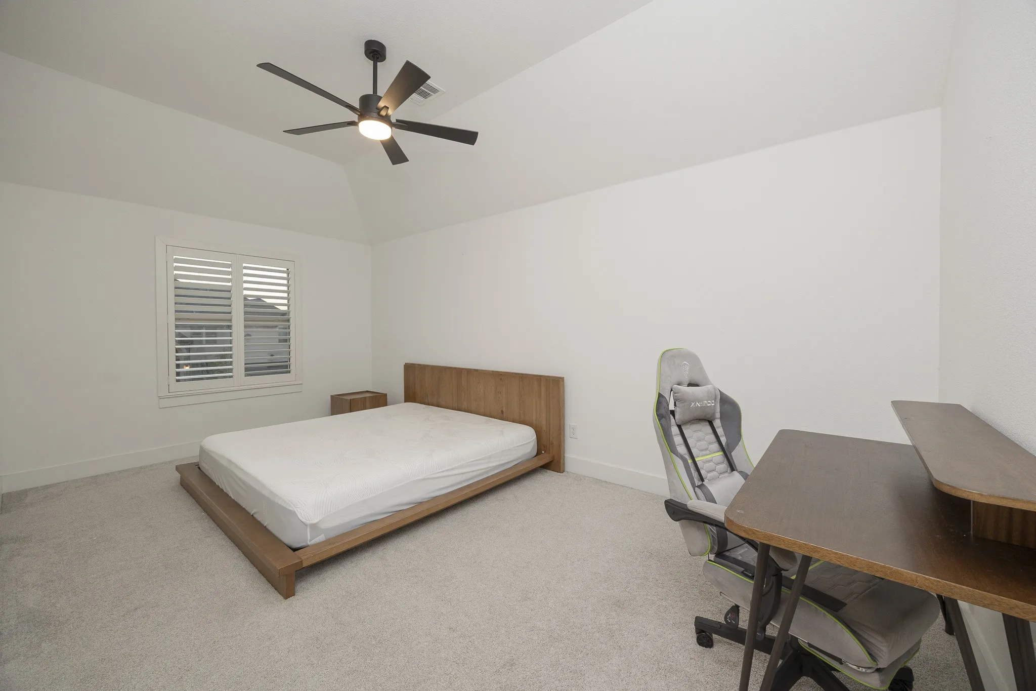 Vaulted ceiling with a ceiling fan, window with plantation shutters, and carpeted flooring