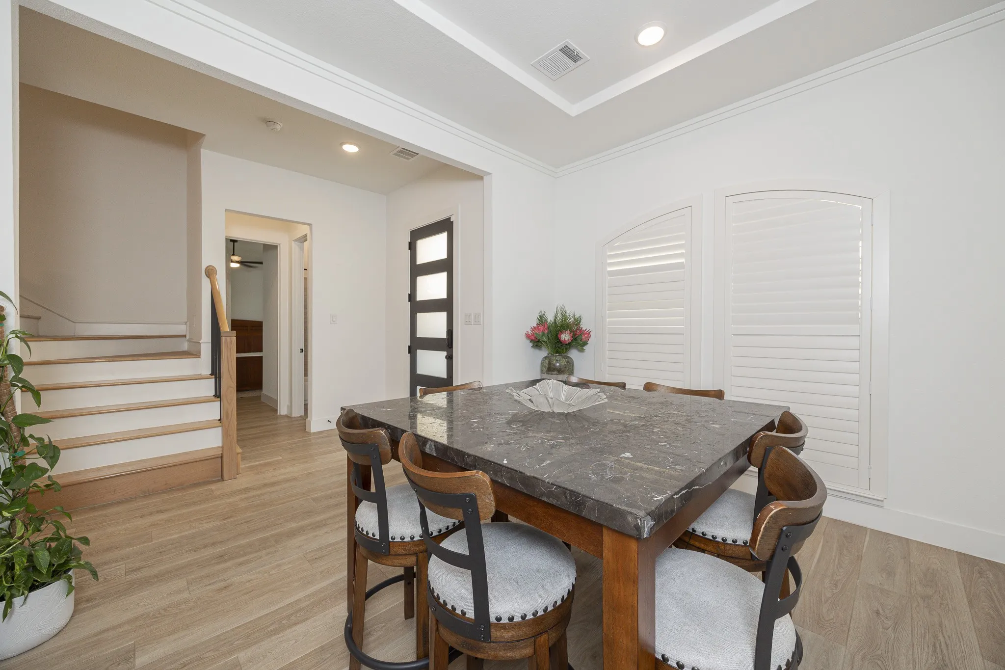 Wood-finish flooring throughout, tray ceiling with recessed lighting, built-in plantation shutters on arched windows, and a black framed door with frosted glass panels