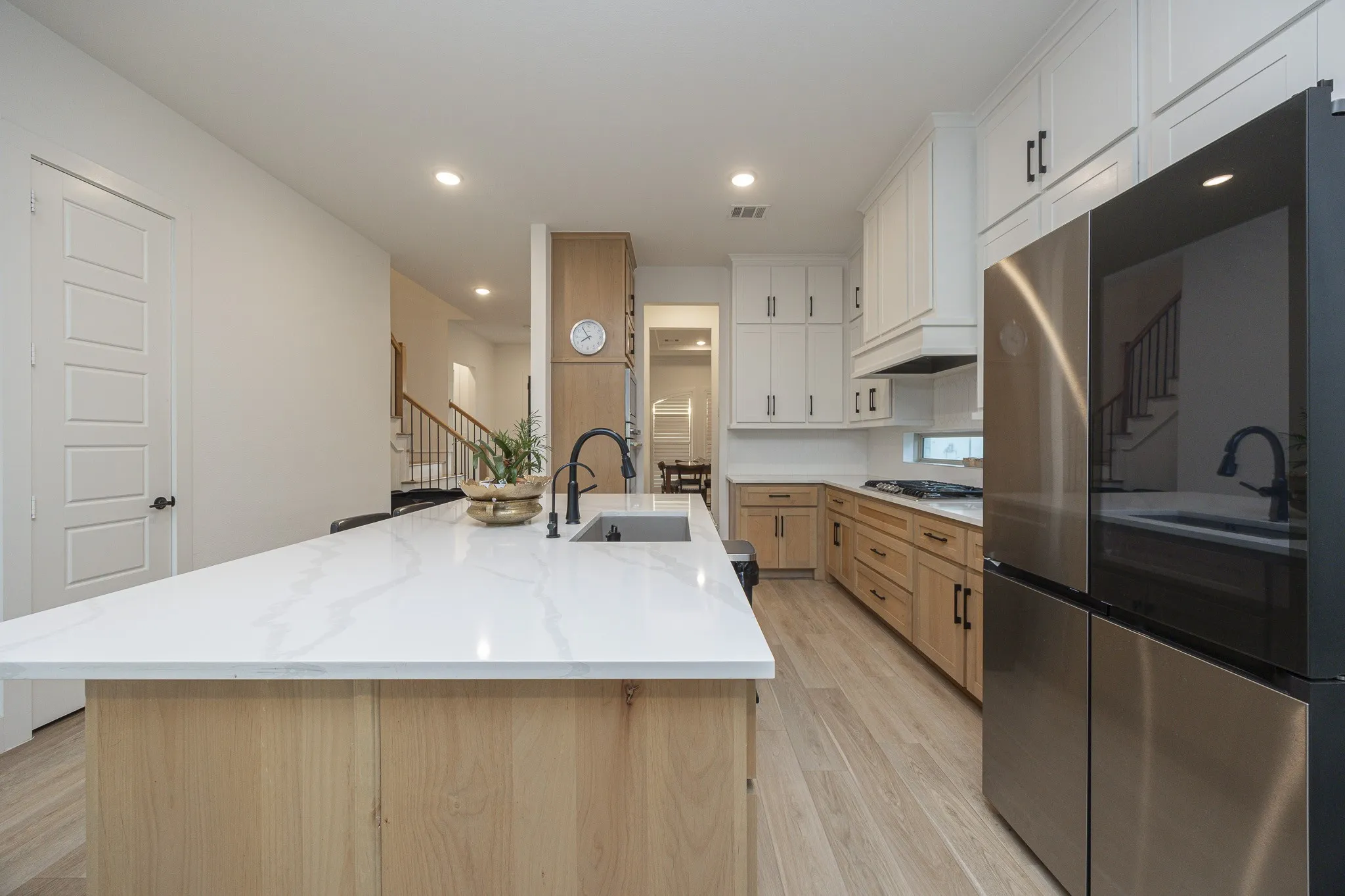 Gourmet kitchen featuring a large central island with a solid surface countertop, wood-finish flooring, stainless steel appliances, and contrasting upper and lower cabinetry