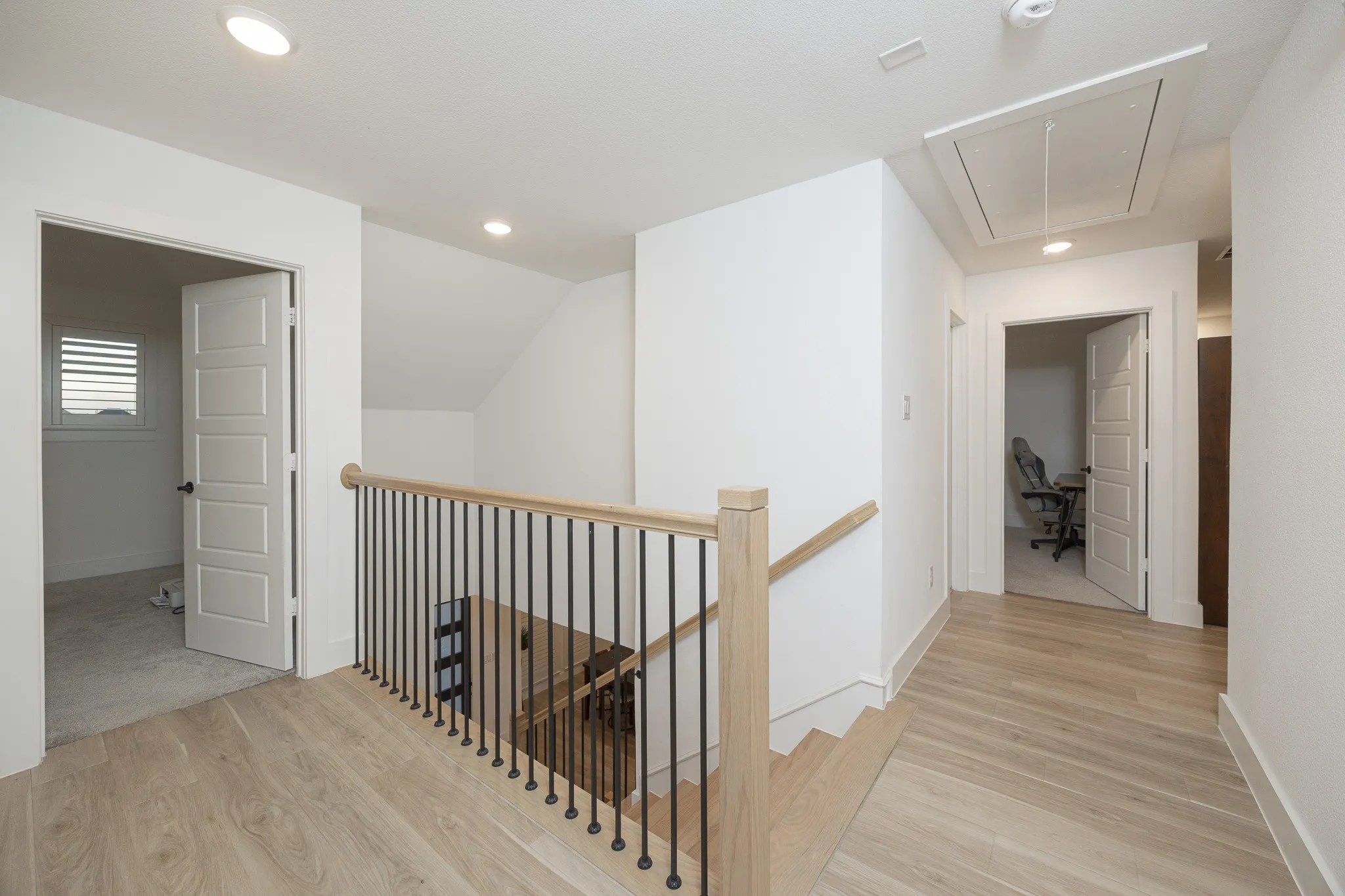 Hardwood-finish flooring, recessed lighting, white panel doors, and a natural wood handrail with black iron balusters