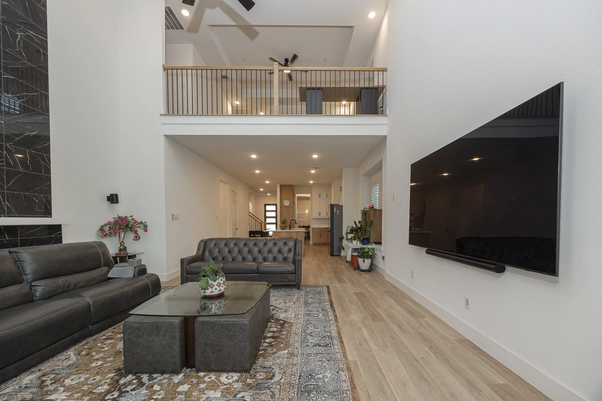 Two-story living area with high ceilings, recessed lighting, a fireplace with a black marble-style surround, and wood-finish flooring