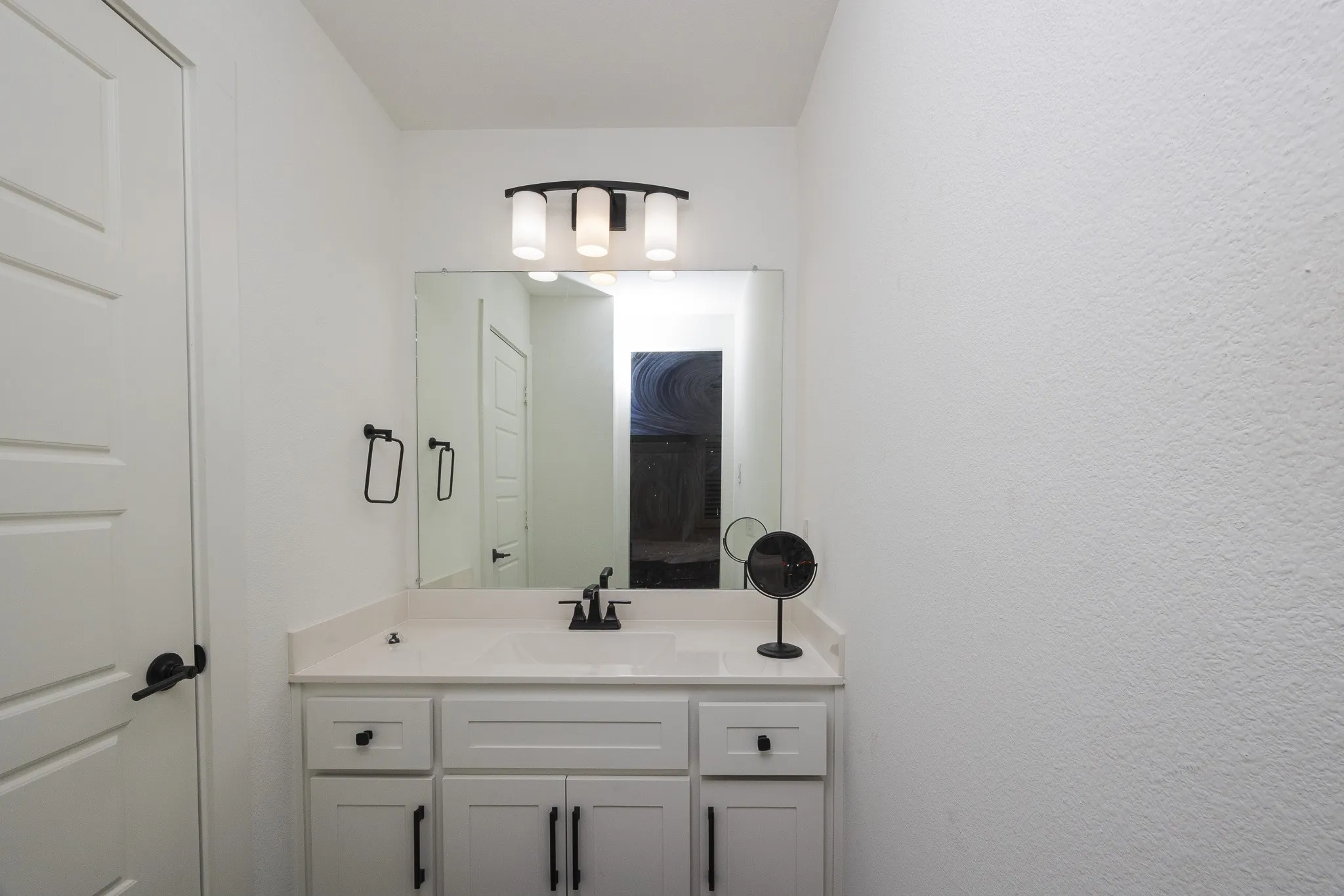 White vanity with shaker-style cabinetry, a built-in rectangular sink, and a light-toned countertop