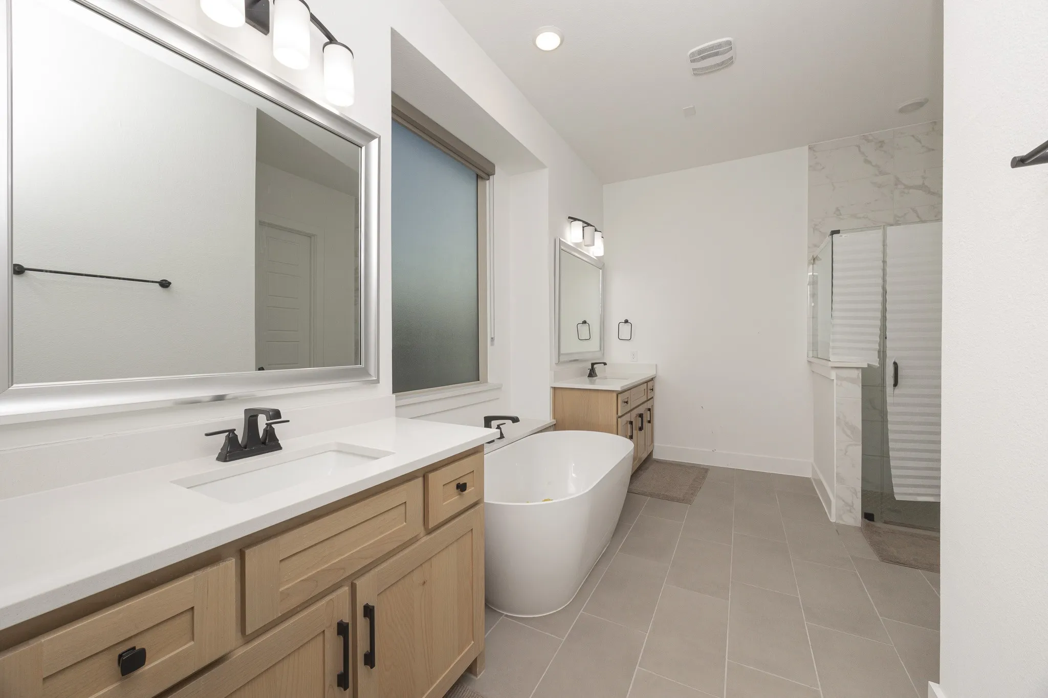 Dual light wood-finish vanities with rectangular undermount sinks, white countertops, and black fixtures