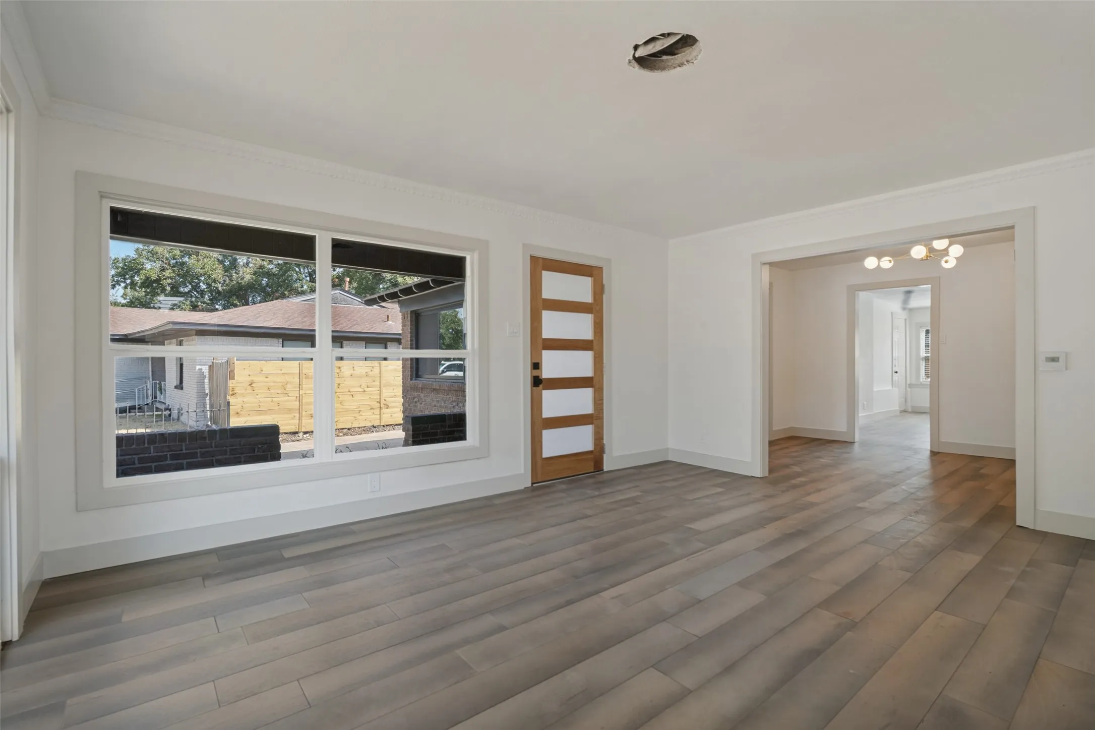 Spacious room featuring wood-finish flooring, a large multi-pane window, and a light wood door with horizontal glass panels